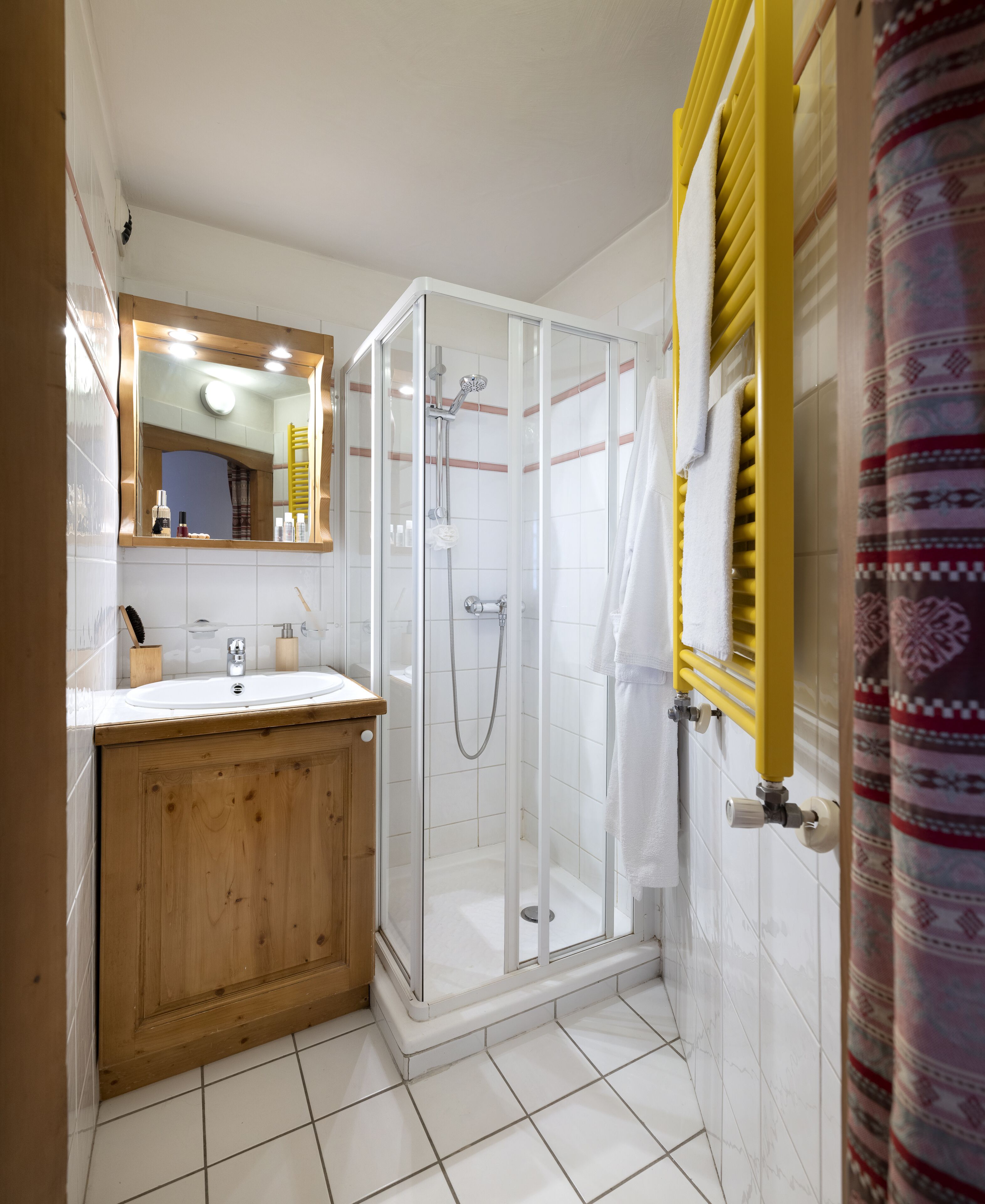A bathroom with a wooden vanity, a glass-enclosed shower, and a yellow towel rack.