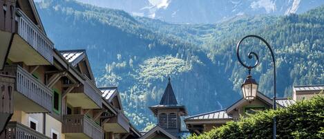 A mountain village with traditional wooden buildings, a bell tower, and a view of snow-capped peaks.