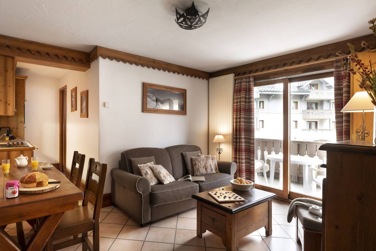 Ein gemütliches Wohnzimmer mit Sofa, Esstisch und einem Balkon mit Aussicht.