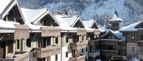 A row of chalet-style buildings with balconies, set against a snowy mountain backdrop.