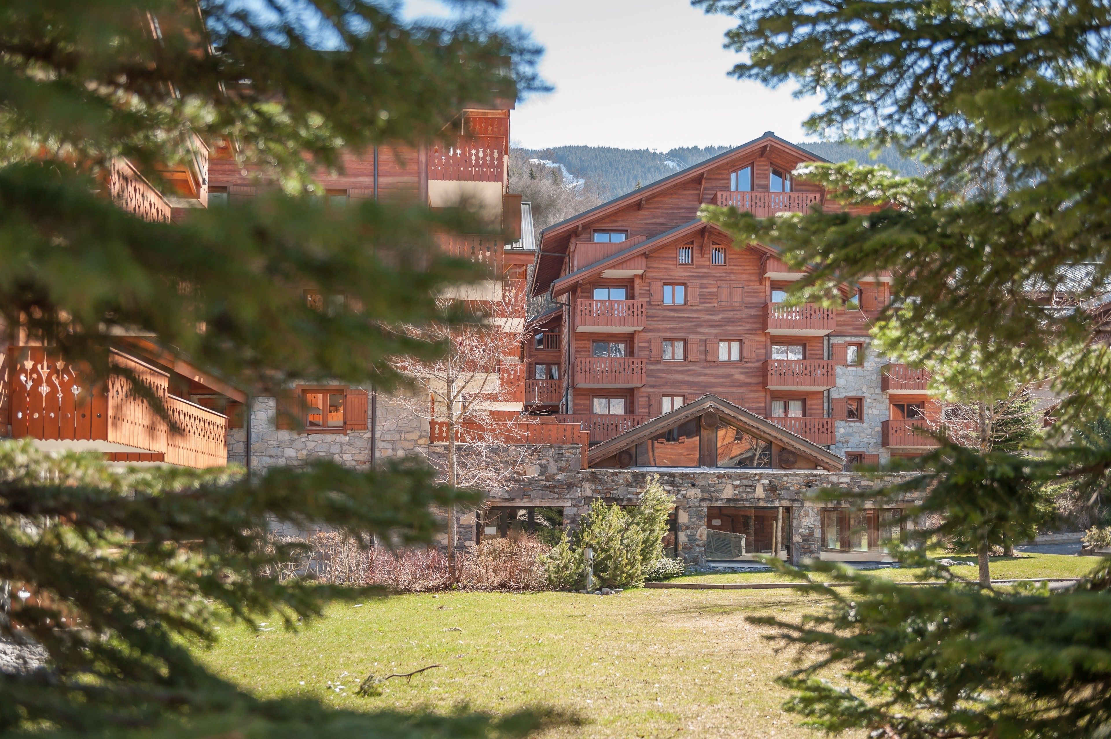 A multi-story wooden building with balconies, surrounded by trees and a grassy area.