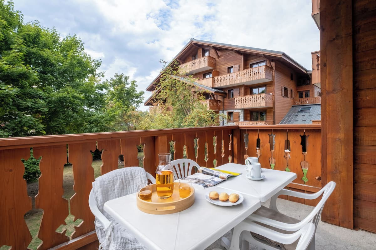 A wooden balcony with a table set for two, a drink tray, and a plate of cookies.