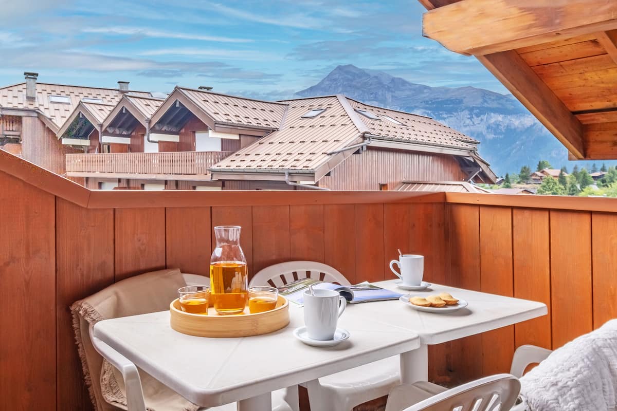 A wooden deck with a table set for breakfast, including a pitcher of tea, a cup, and a plate of cookies.