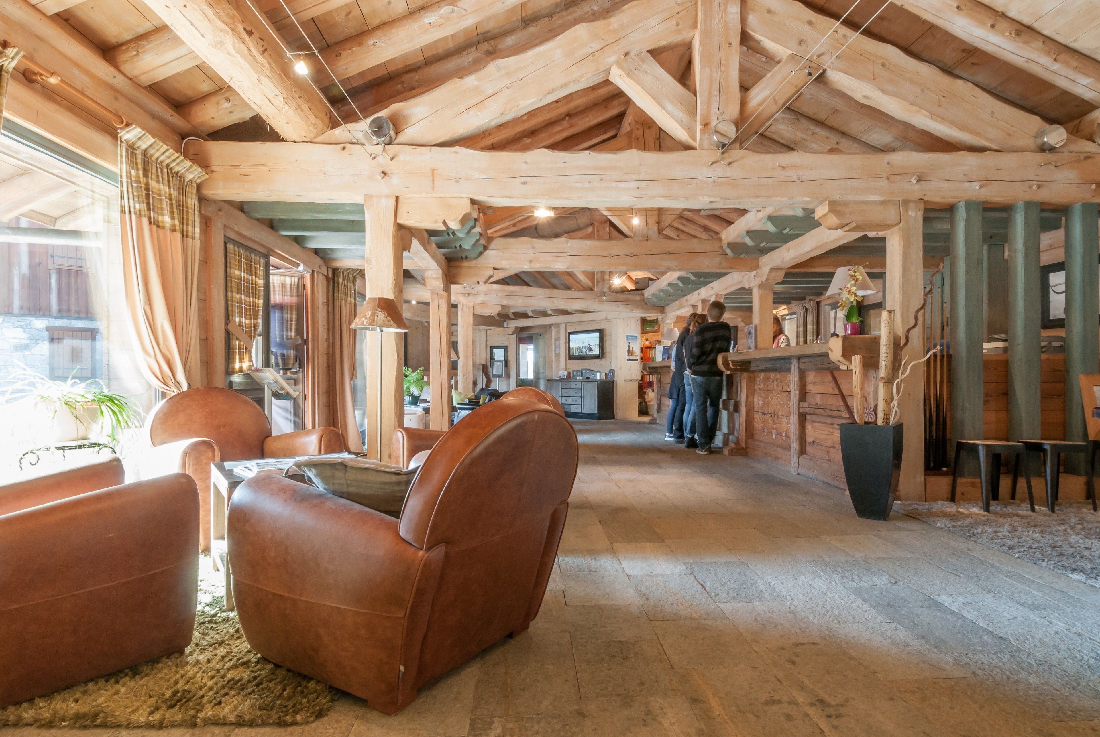 A spacious interior with wooden beams, leather seating, and a kitchen area in the background.