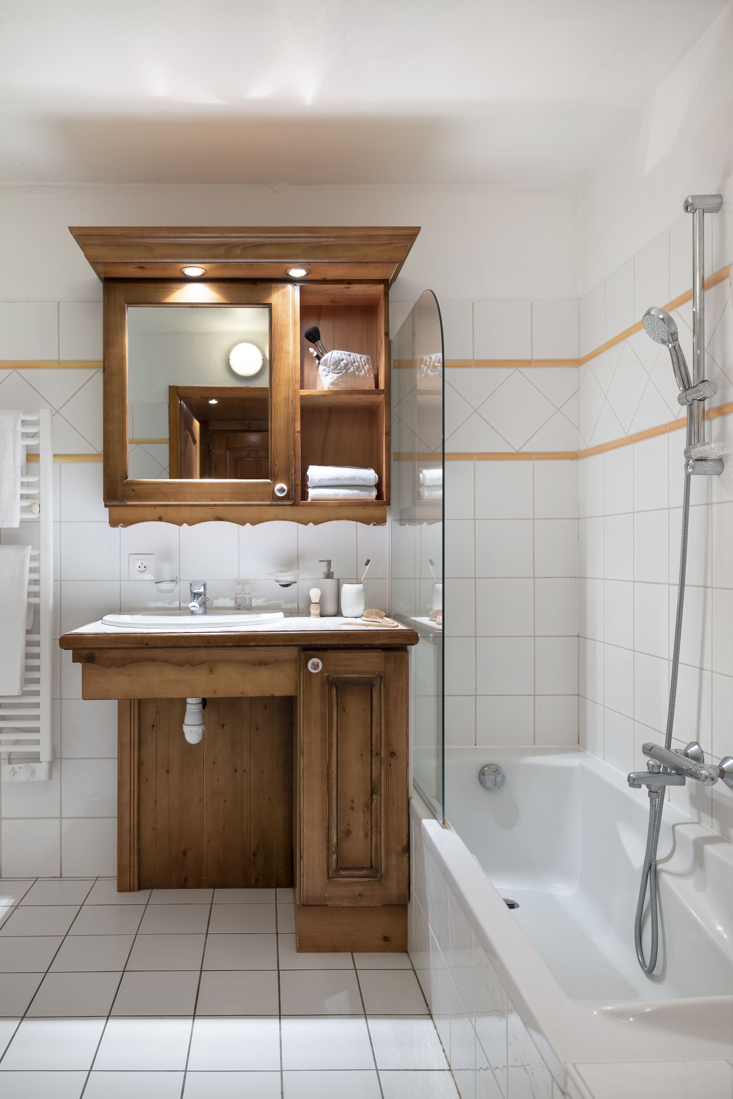 A modern bathroom with a wooden vanity, a glass shower enclosure, and a white tiled floor.