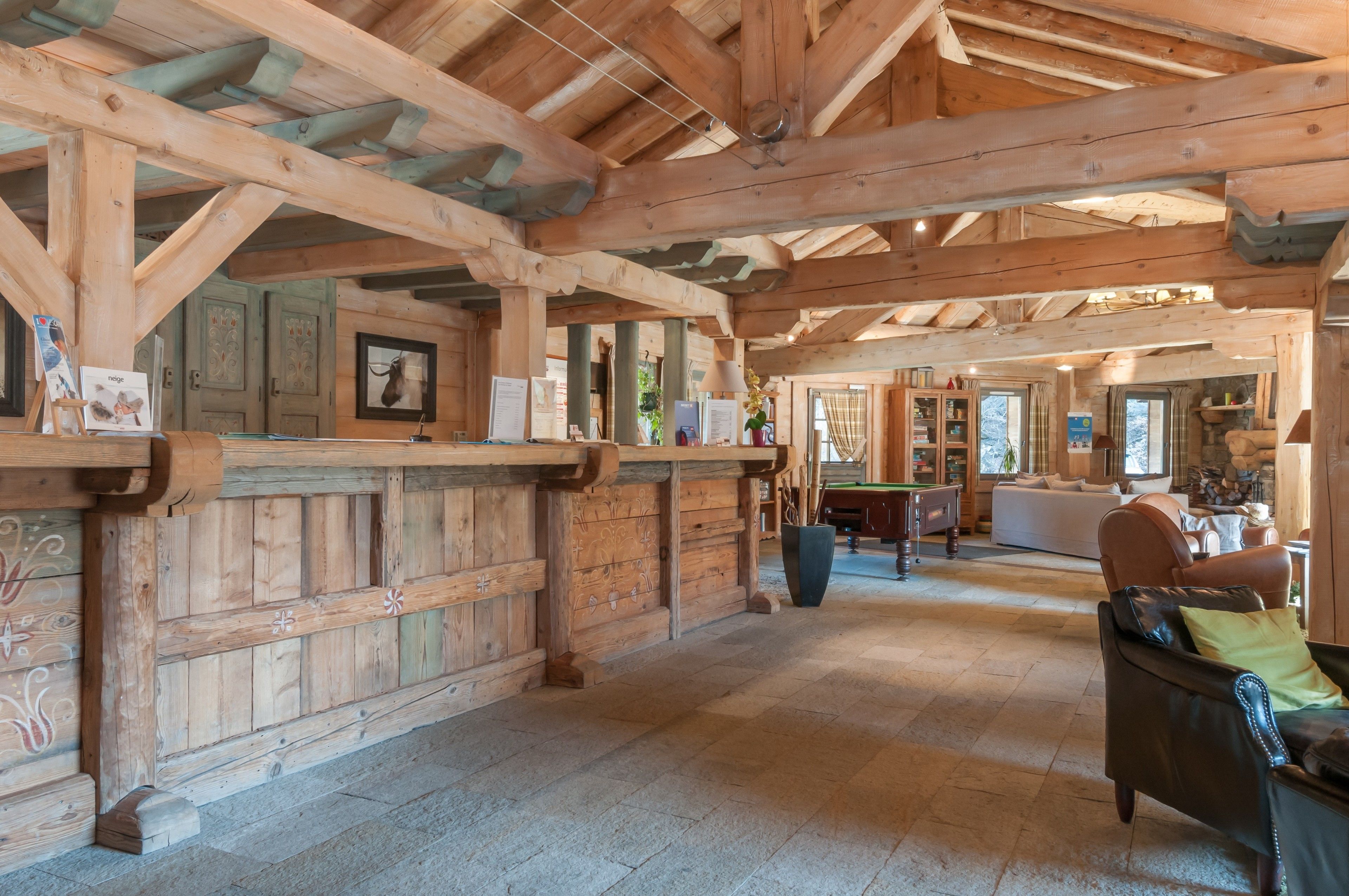 A spacious wooden interior with a high ceiling and exposed beams, featuring a billiards table, a sofa, and a dining area.