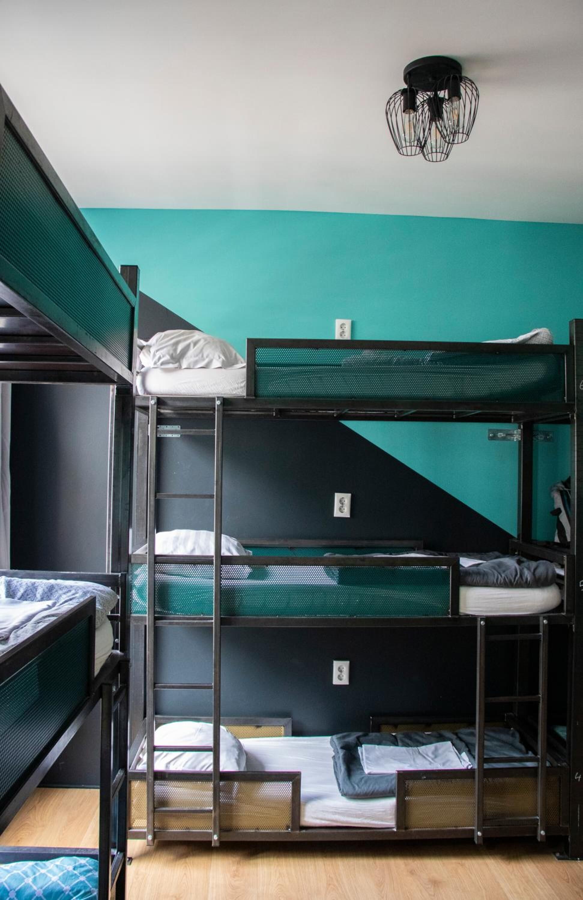 A bunk bed room with a teal wall, a black ceiling light, and a wooden floor.