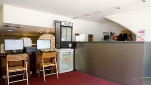 A reception area with two wooden chairs, a refrigerator, a Coca-Cola vending machine, and a computer desk with two monitors. - Marnix Hotel (Amsterdam)