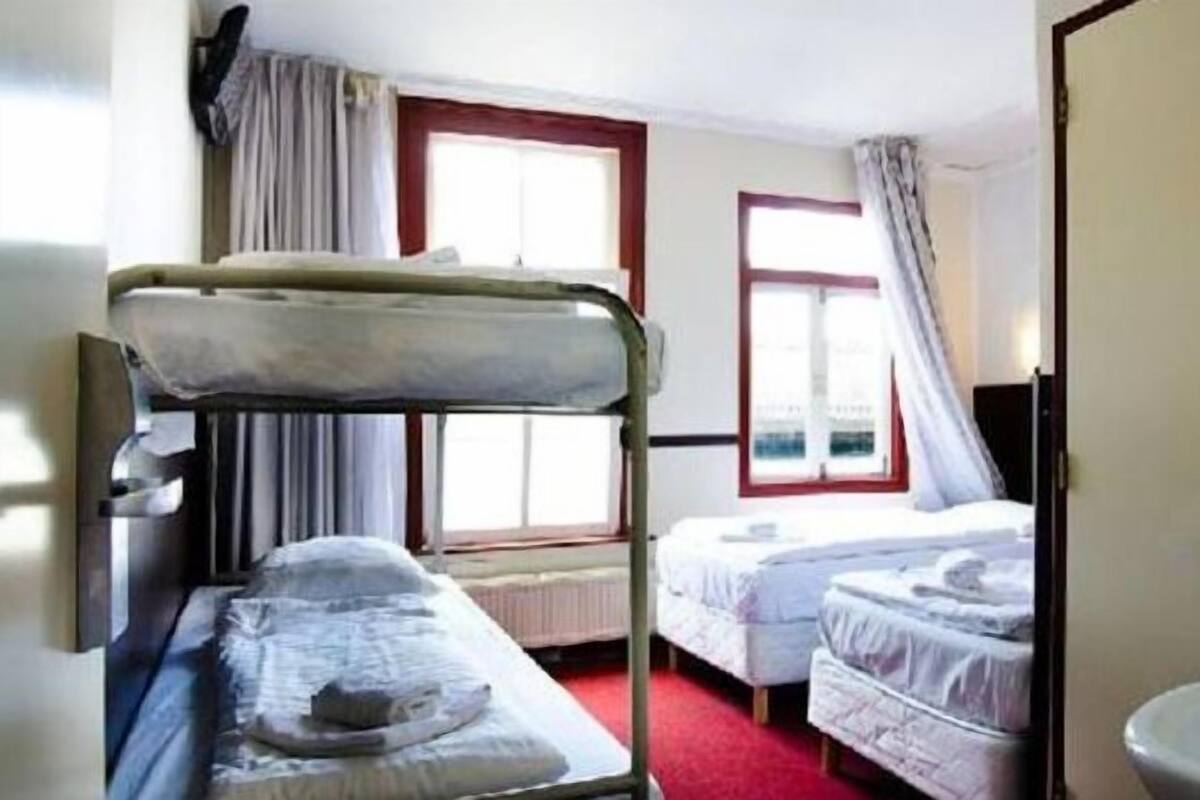 Una habitación con literas, una ventana con cortinas y un radiador.
