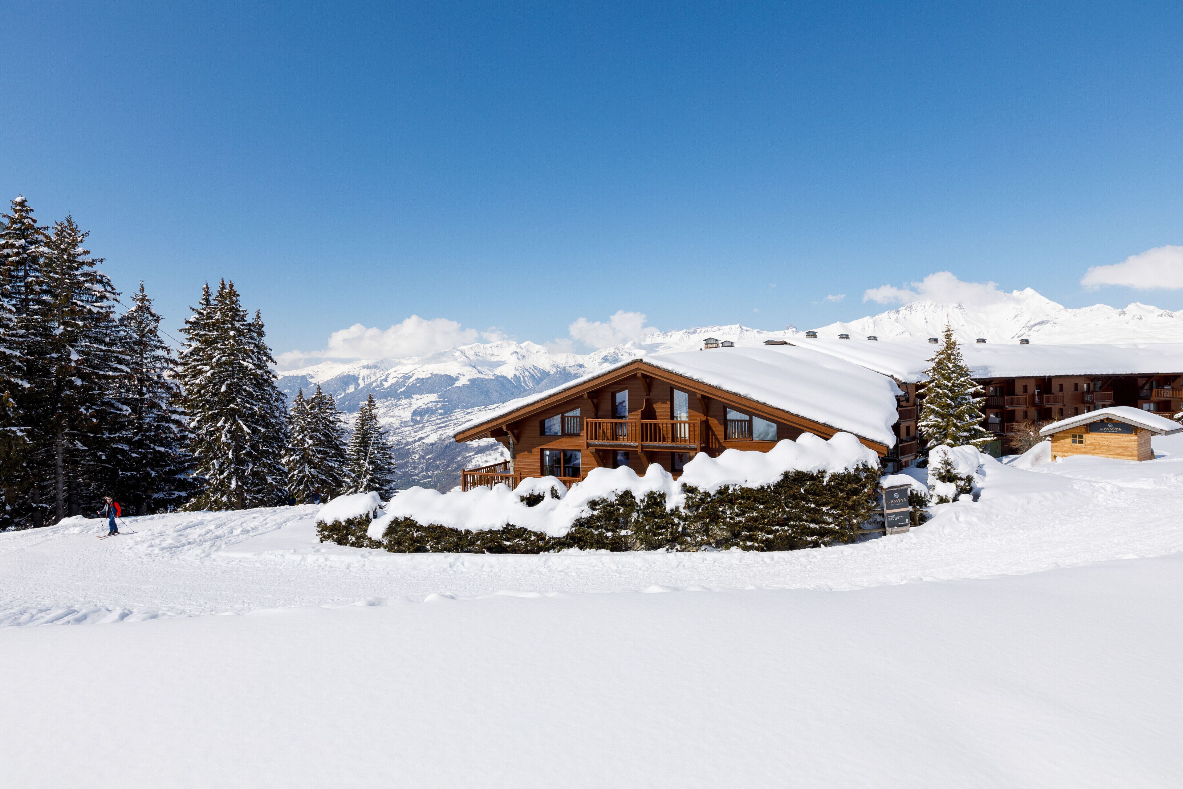 Un chalet en bois, dont le toit est recouvert de neige, entouré d’arbres et de montagnes enneigés.
