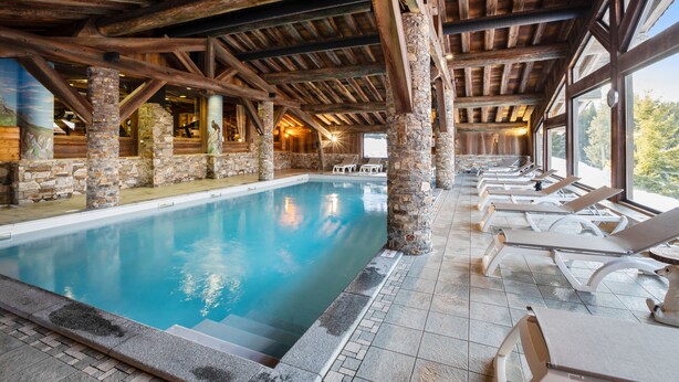 An indoor swimming pool with stone pillars, wooden beams, and lounge chairs. - Résidence Pierre & Vacances Premium Les Alpages de Chantel (Bourg-Saint-Maurice)