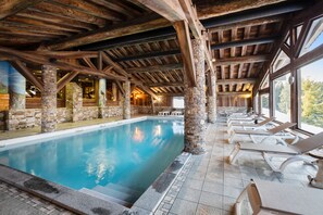 An indoor swimming pool with stone pillars, wooden beams, and lounge chairs.