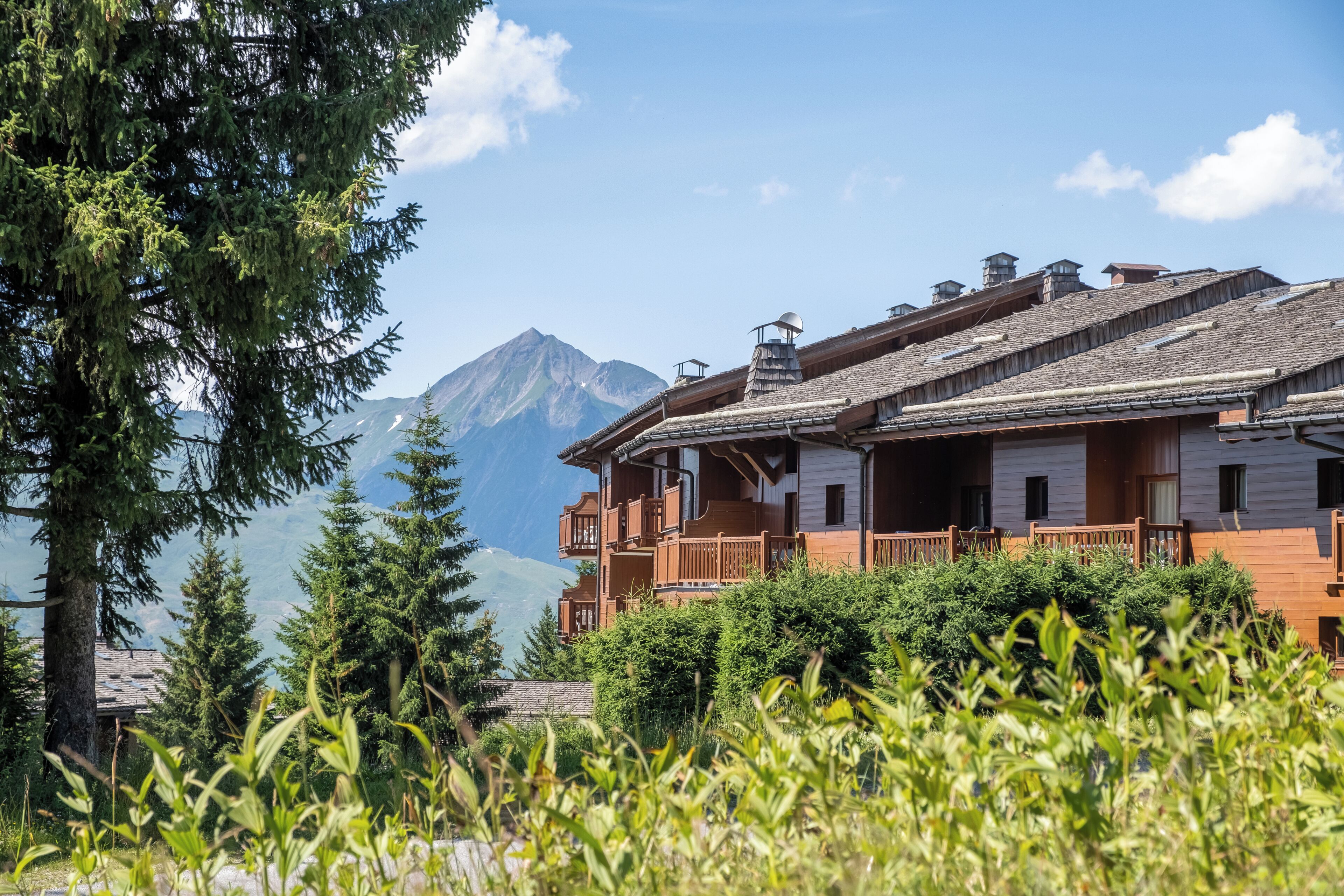 A chalet-style building with a wooden facade, multiple balconies, and a mountain backdrop.
