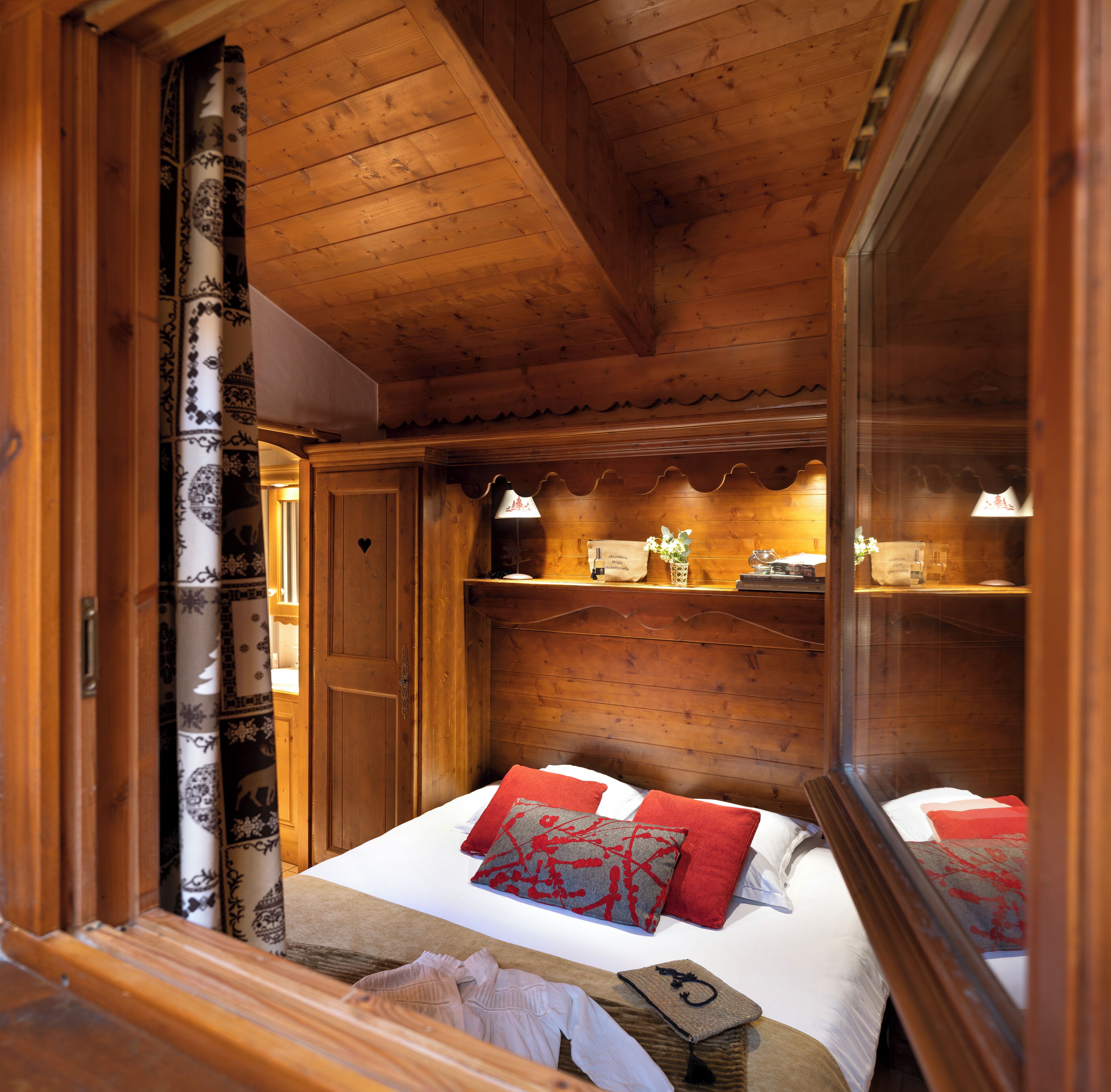 A wooden cabin bedroom with a bed, pillows, a nightstand, and a dresser.