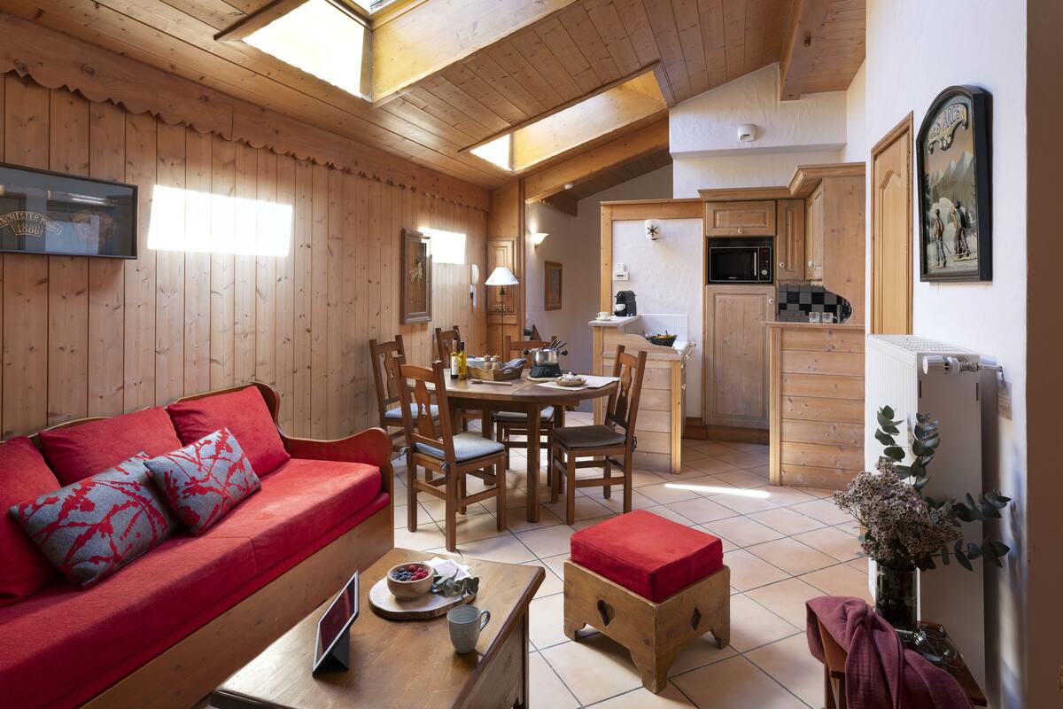 Una habitación acogedora con techo de madera, un sofá rojo, una mesa de comedor con sillas y una zona de cocina con armarios de madera.