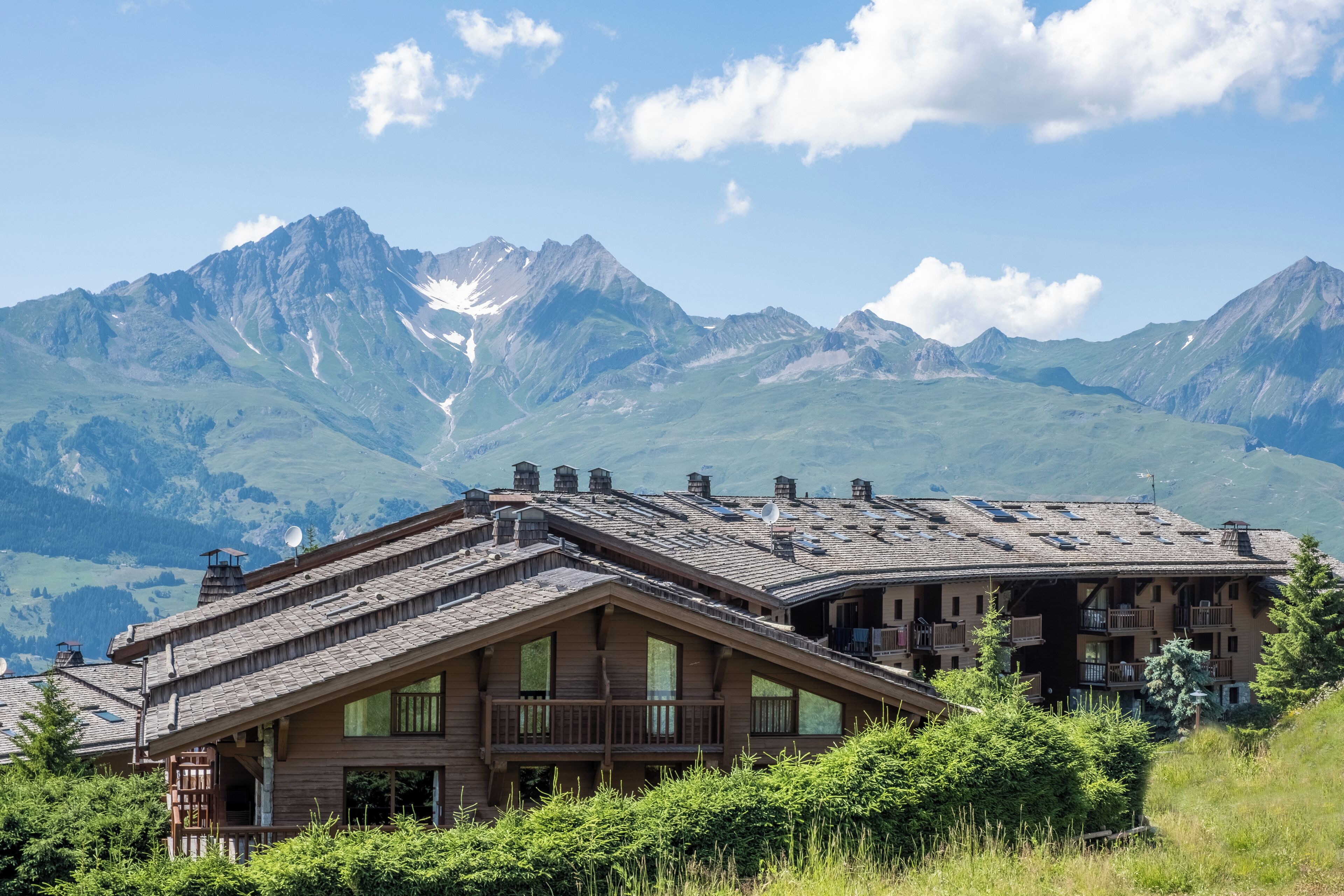 A mountain lodge with a sloped roof, balconies, and a view of snow-capped mountains.