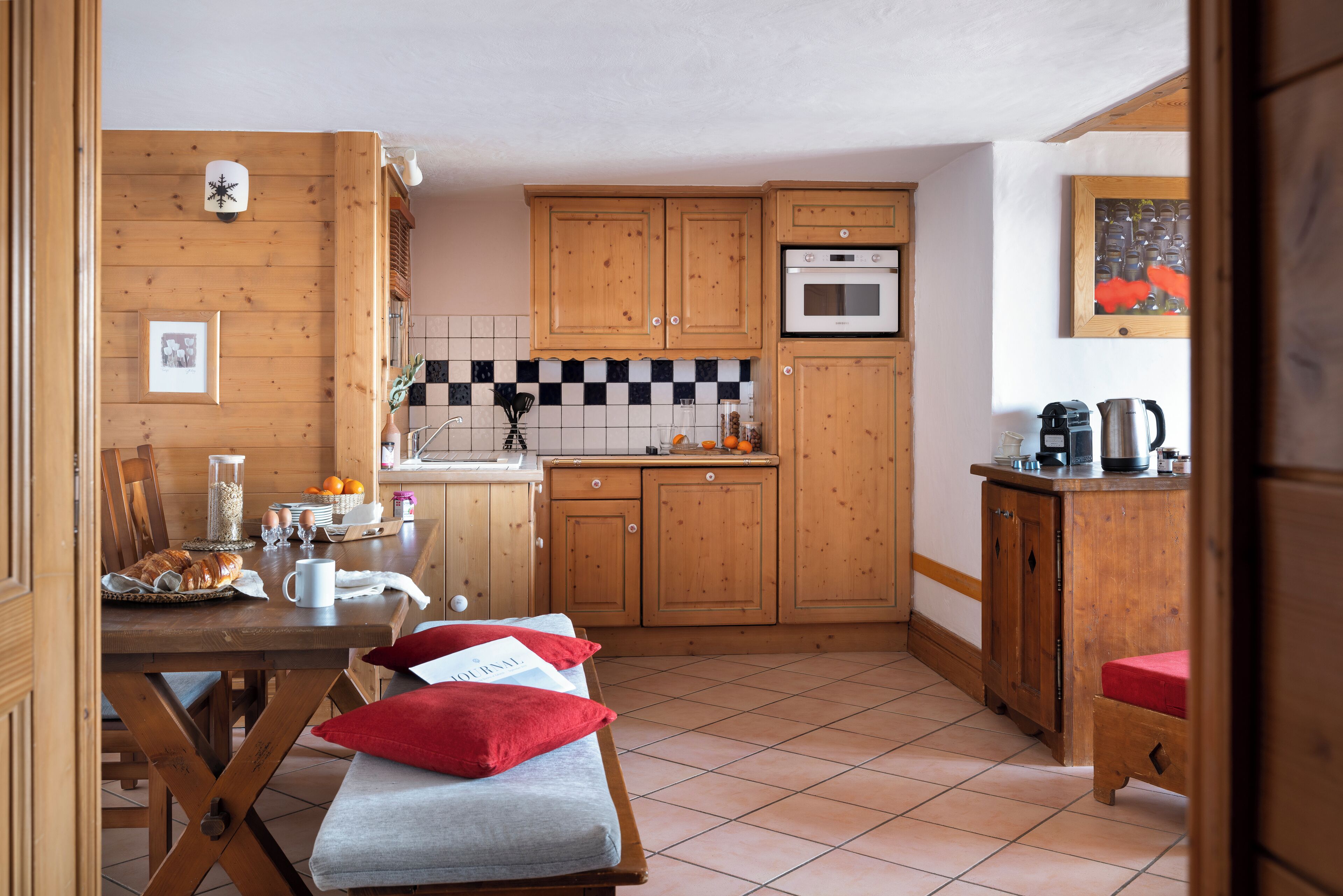 Une cuisine chaleureuse avec des meubles en bois, un dosseret carrelé et un coin repas comprenant un banc et des coussins.