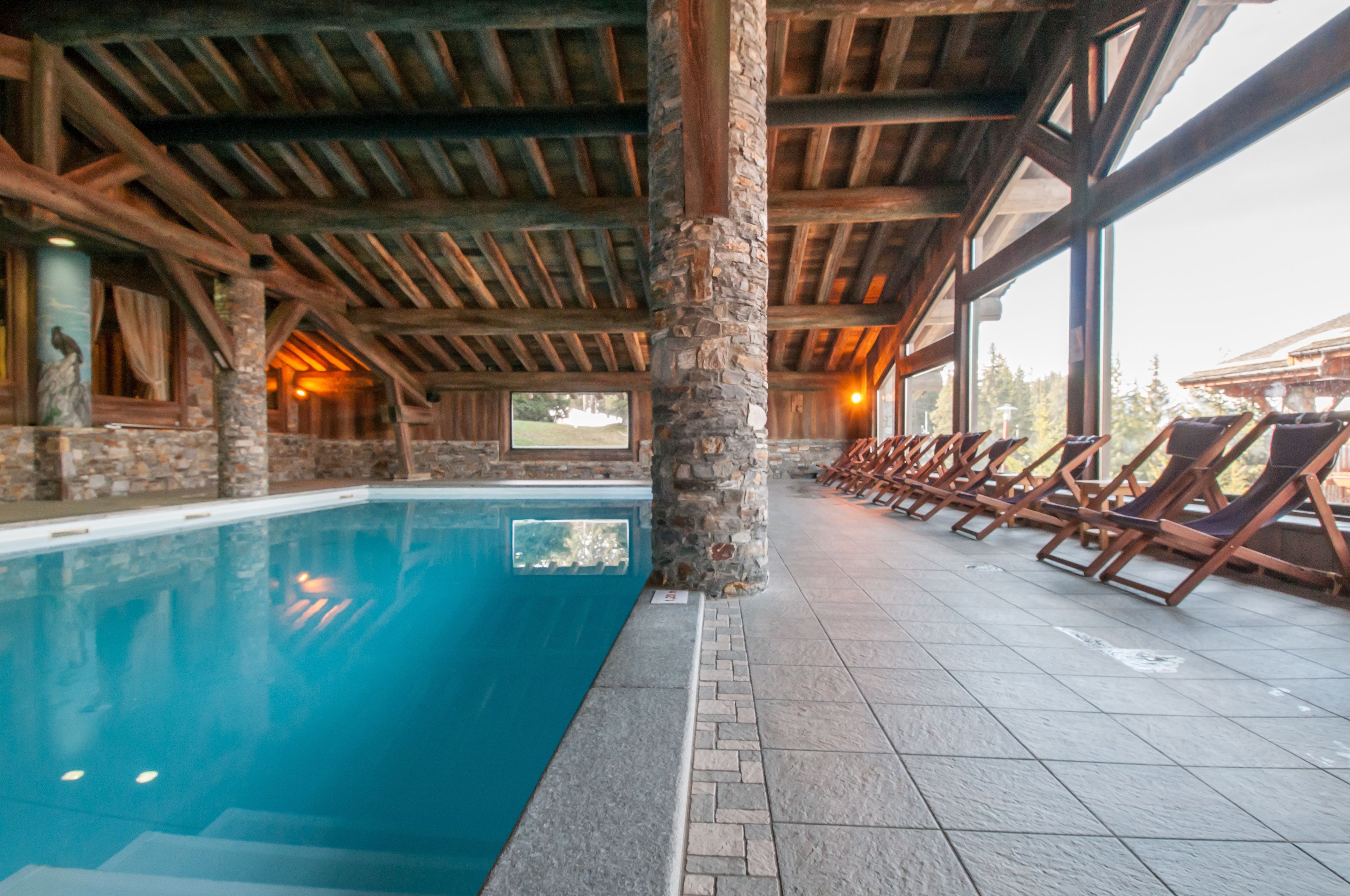 Une piscine intérieure agrémentée de piliers en pierre, de poutres en bois et de chaises longues disposées le long des bords.