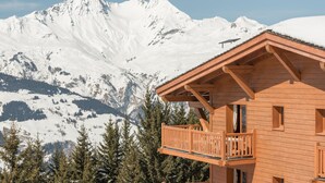 A wooden chalet with a balcony, set against a backdrop of snow-covered mountains. - Résidence Pierre & Vacances Premium Les Alpages de Chantel (Bourg-Saint-Maurice)