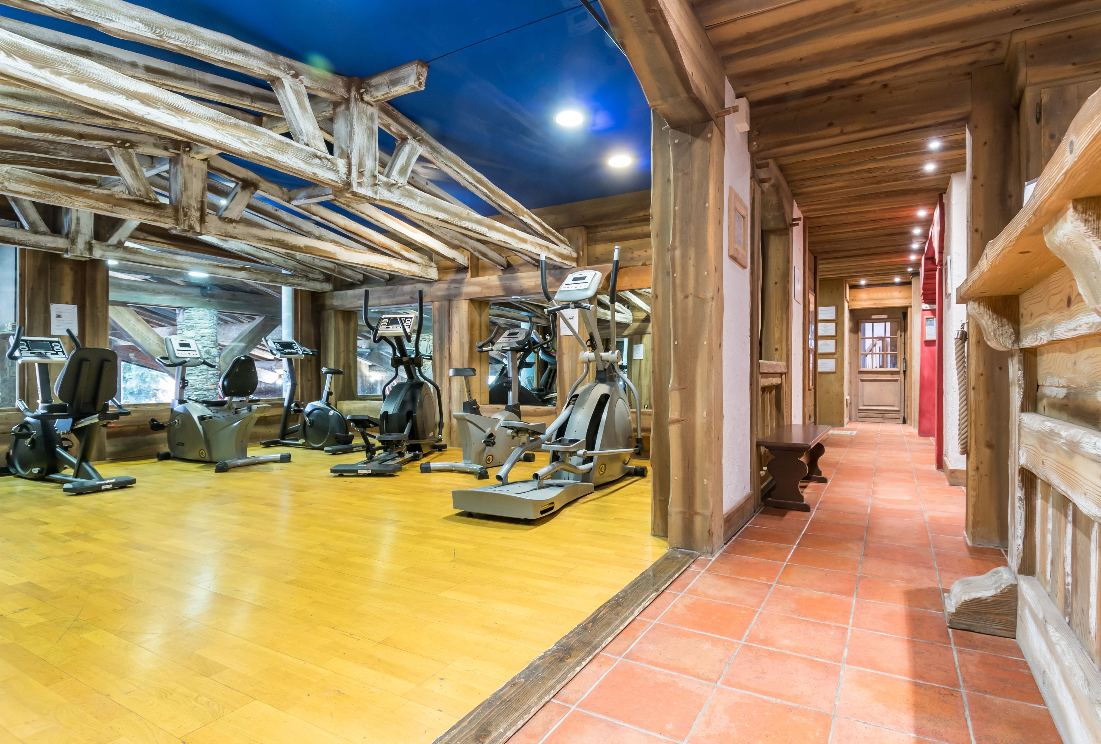 A gym with various exercise machines, wooden walls, and a tiled floor.