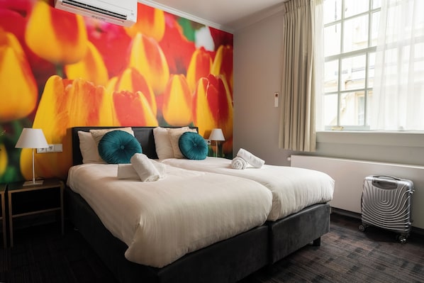 Habitación de hotel con una cama grande, dos mesitas de noche con lámparas, un radiador y una ventana con cortinas.