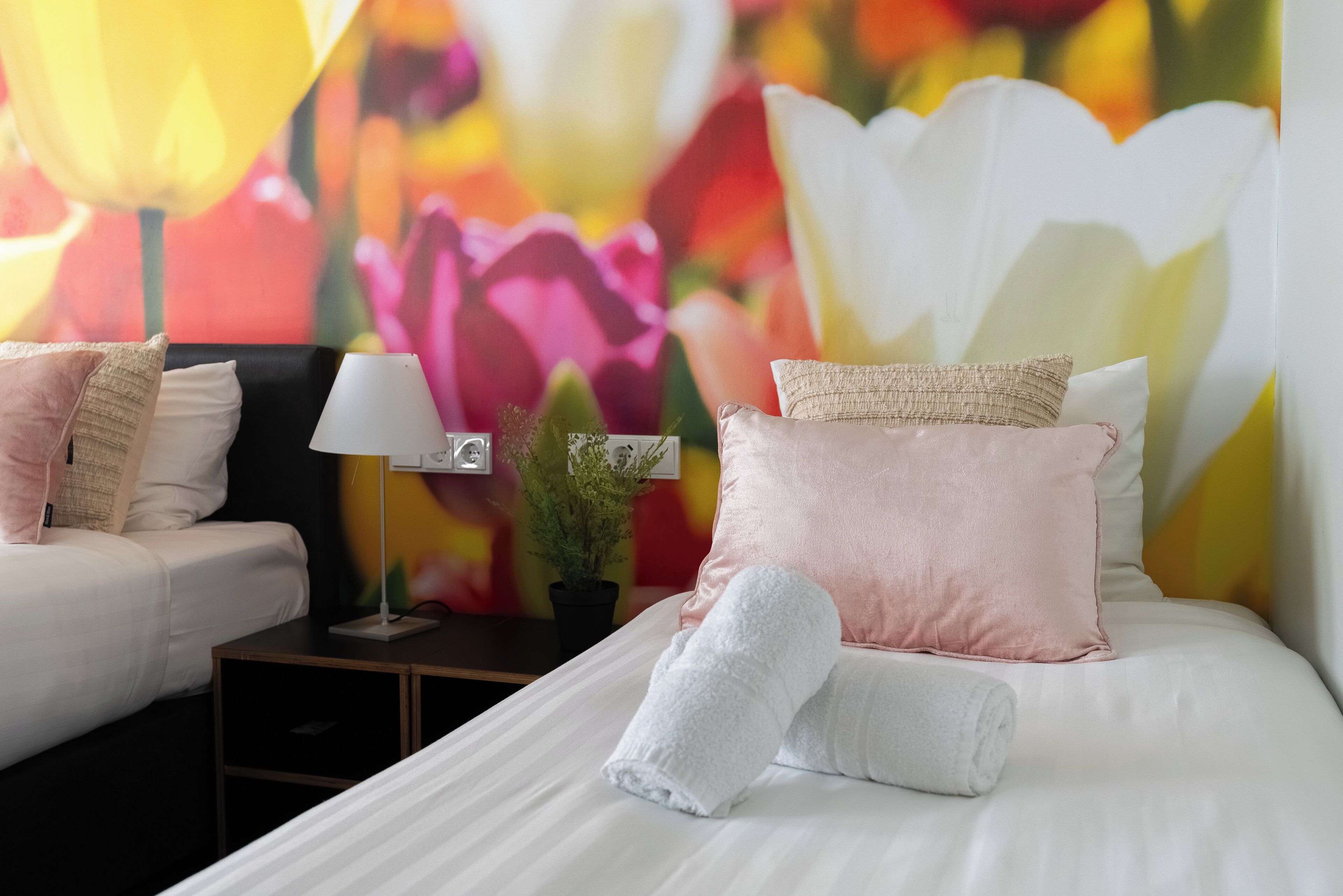 A hotel room with a bed, a nightstand, a lamp, and a wall with a floral mural.