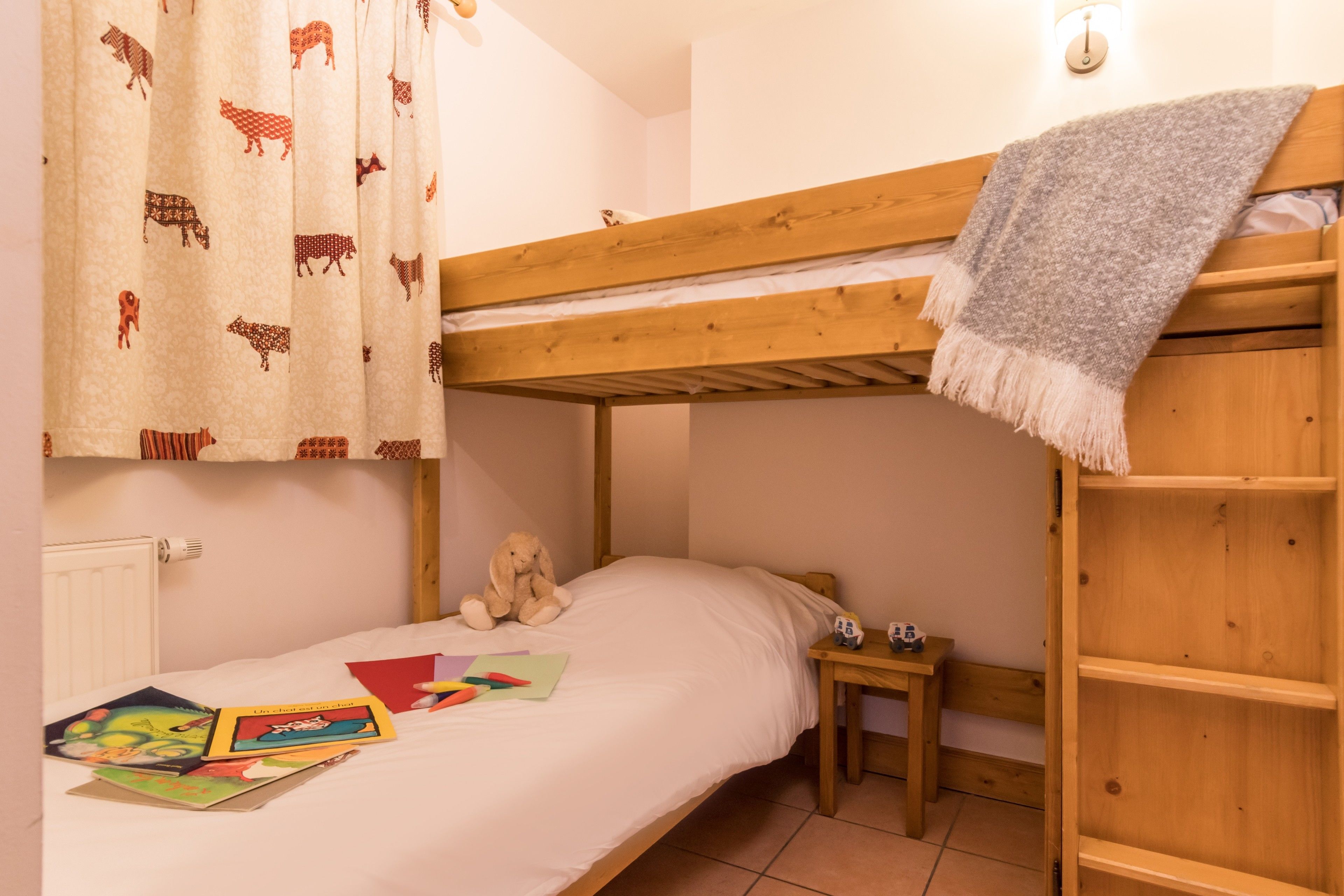 Een slaapkamer met een stapelbed, een houten hoofdbord, een klein nachtkastje met een lamp en een gordijn met dierenprint.