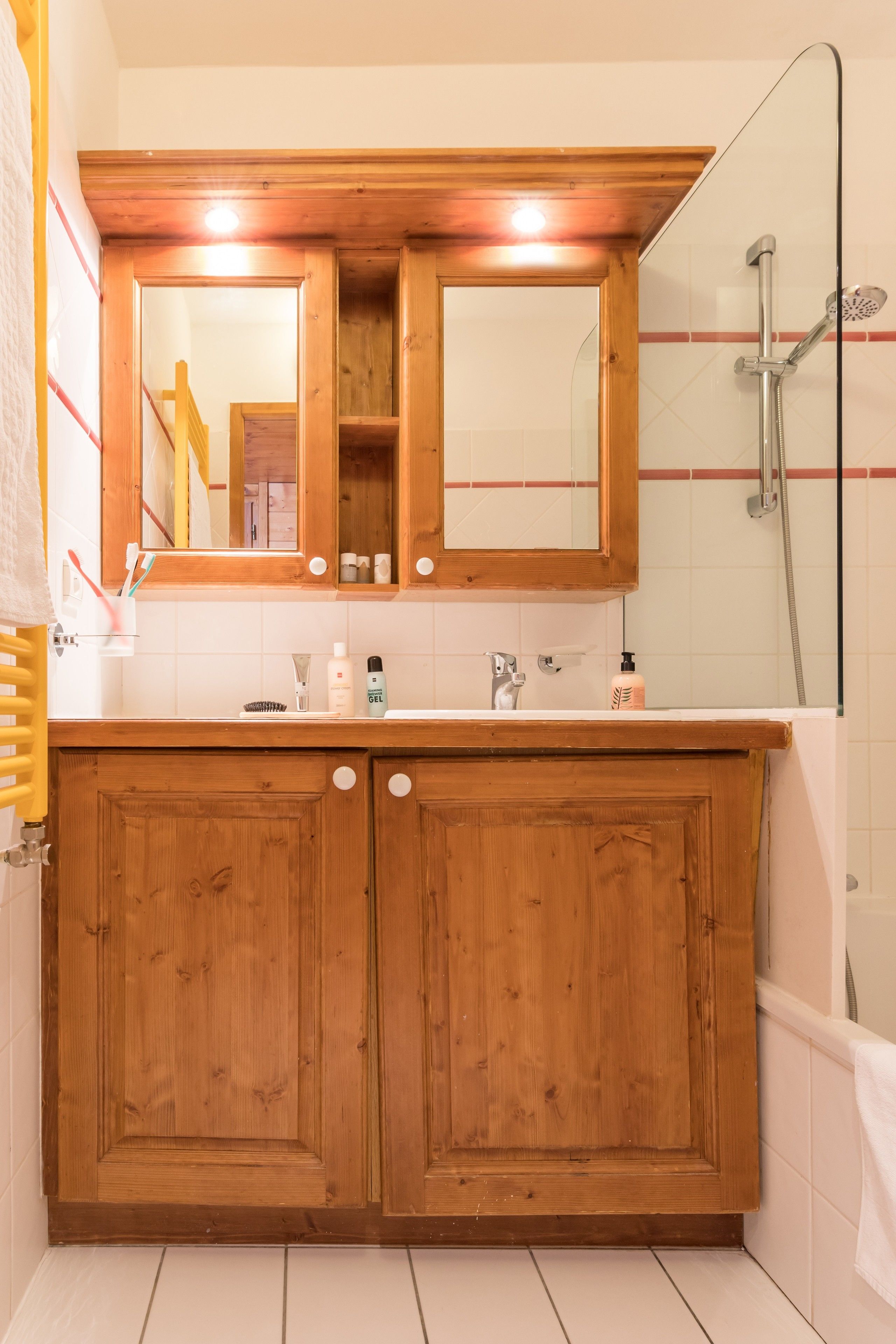 Une coiffeuse en bois avec un miroir, une douche et un mur recouvert de carreaux blancs.