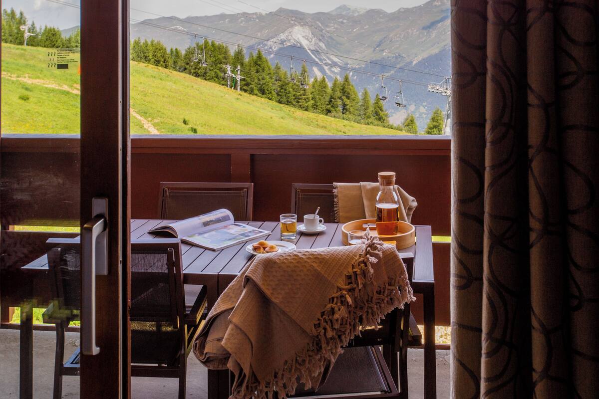 Une table à manger avec vue sur les montagnes, une bouteille et une tasse.