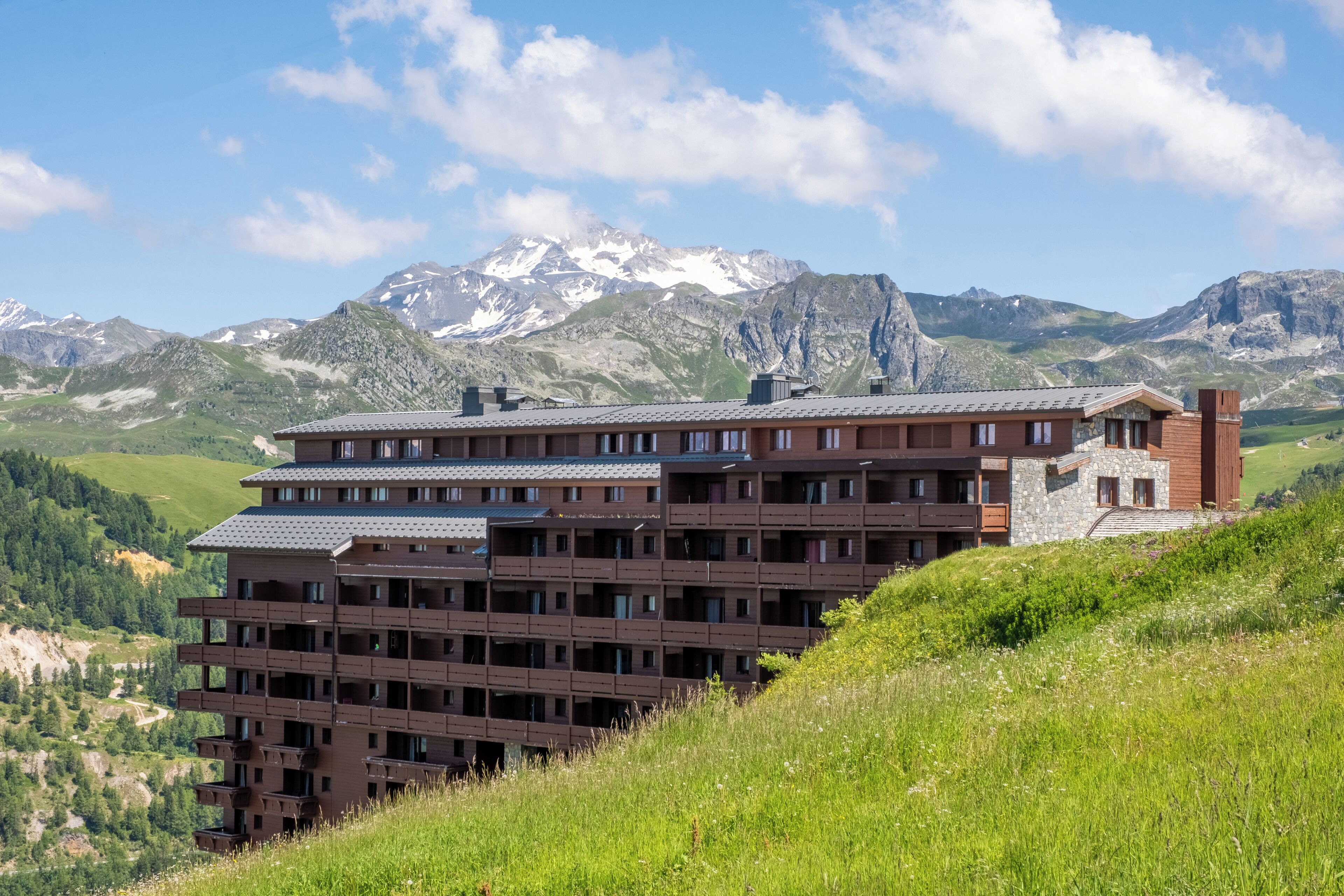 Un hotel de varios pisos con un diseño moderno, ubicado en una colina con montañas al fondo.
