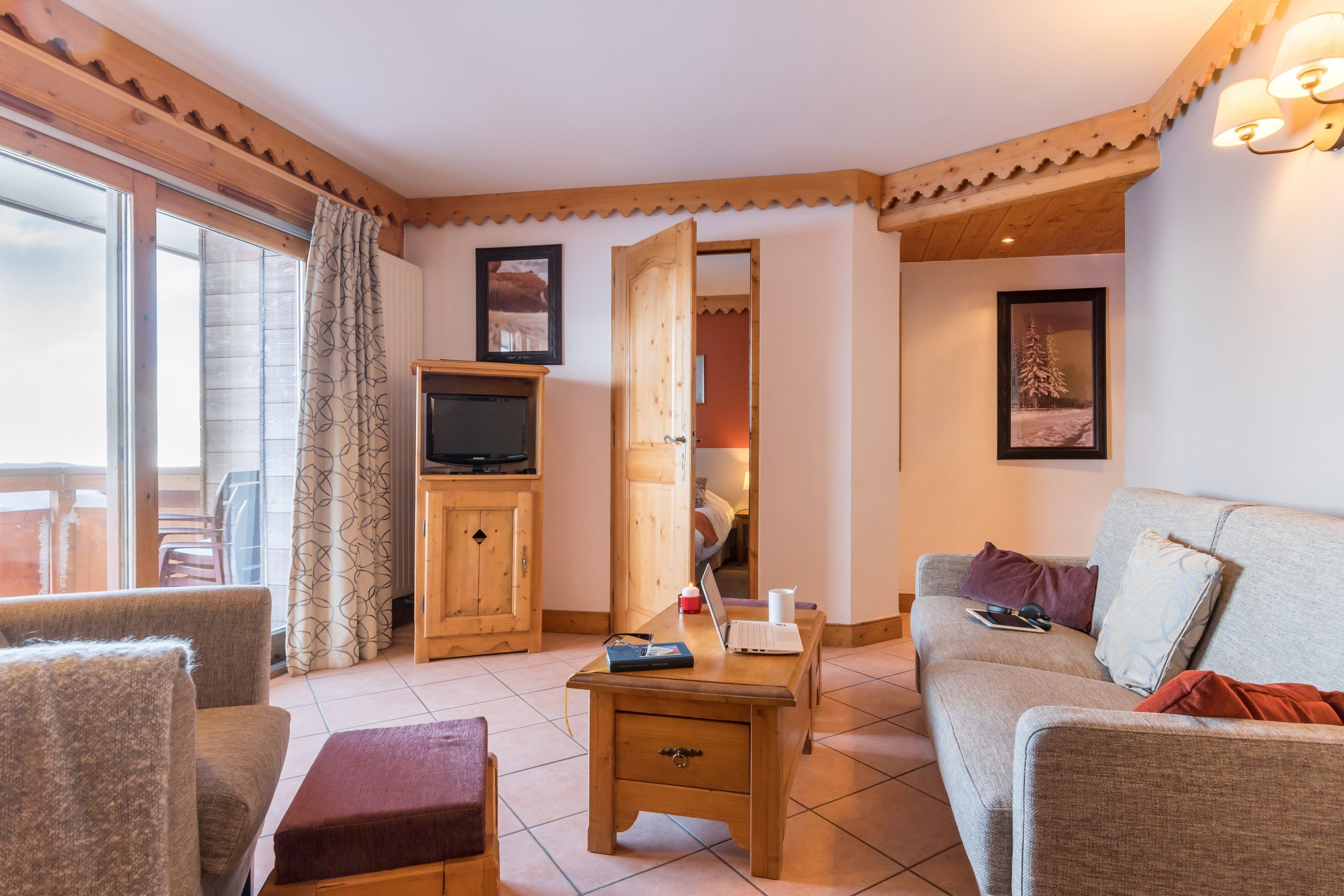 Una sala de estar acogedora con un sofá, una mesa de centro de madera, un televisor en un mueble y una puerta que da a otra habitación.
