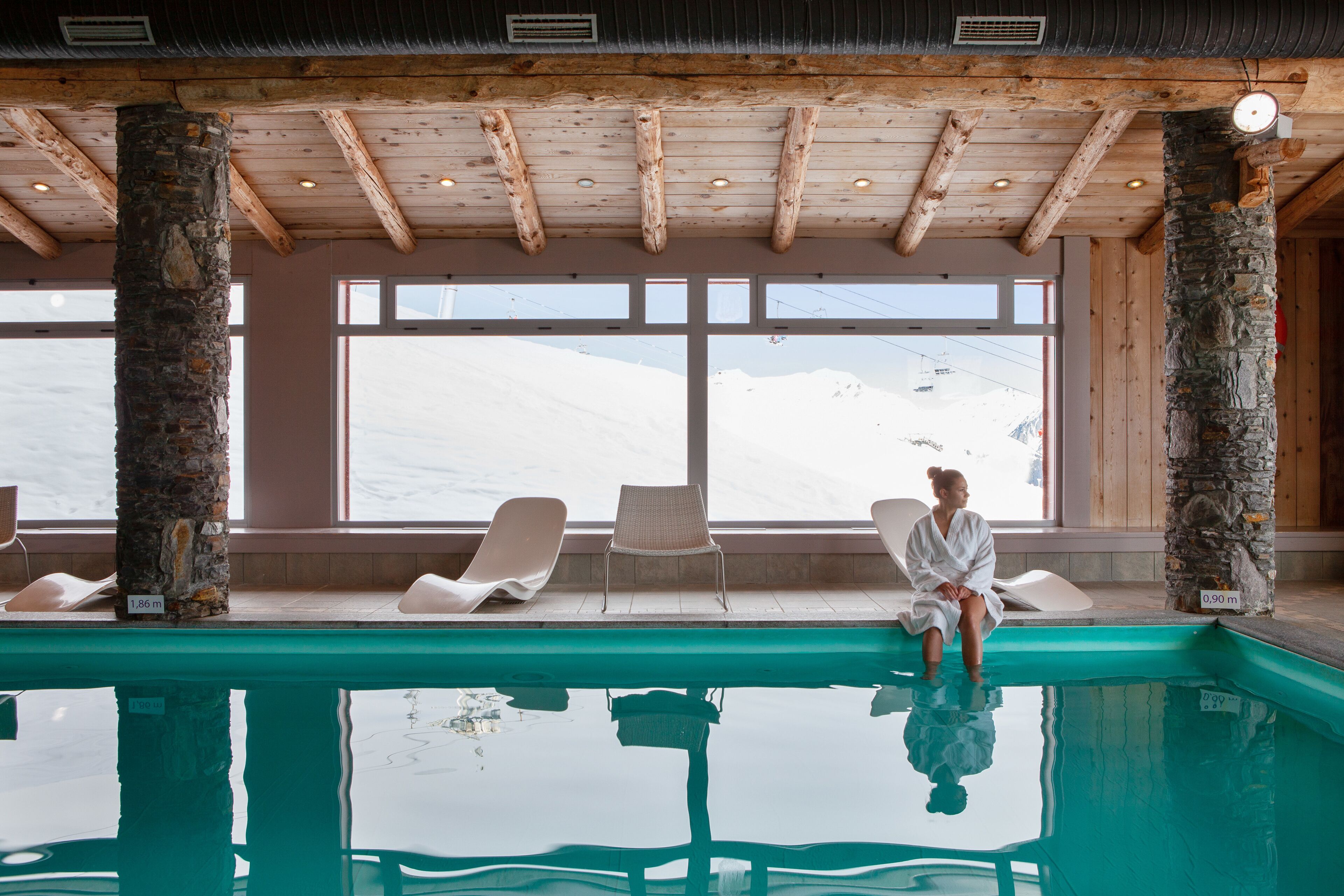 A pool area with wooden beams, stone pillars, and lounge chairs.
