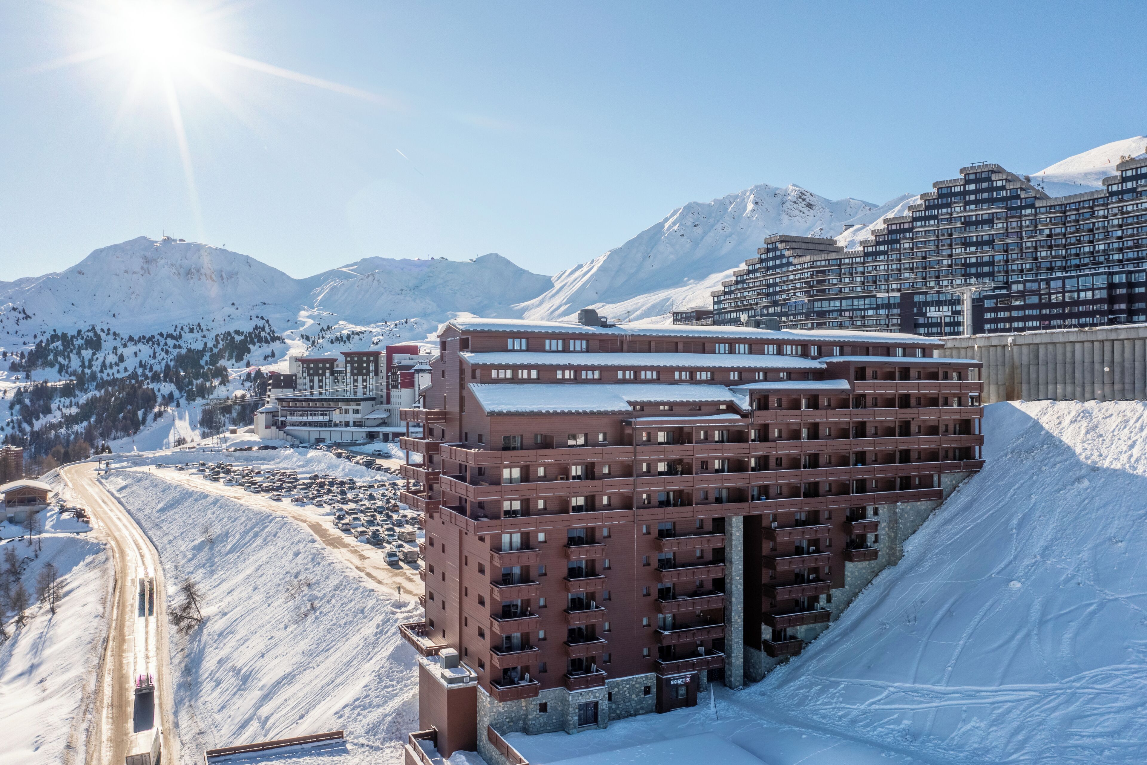 Ein mehrstöckiges Hotel mit schneebedecktem Dach in einer Berglandschaft unter blauem Himmel.