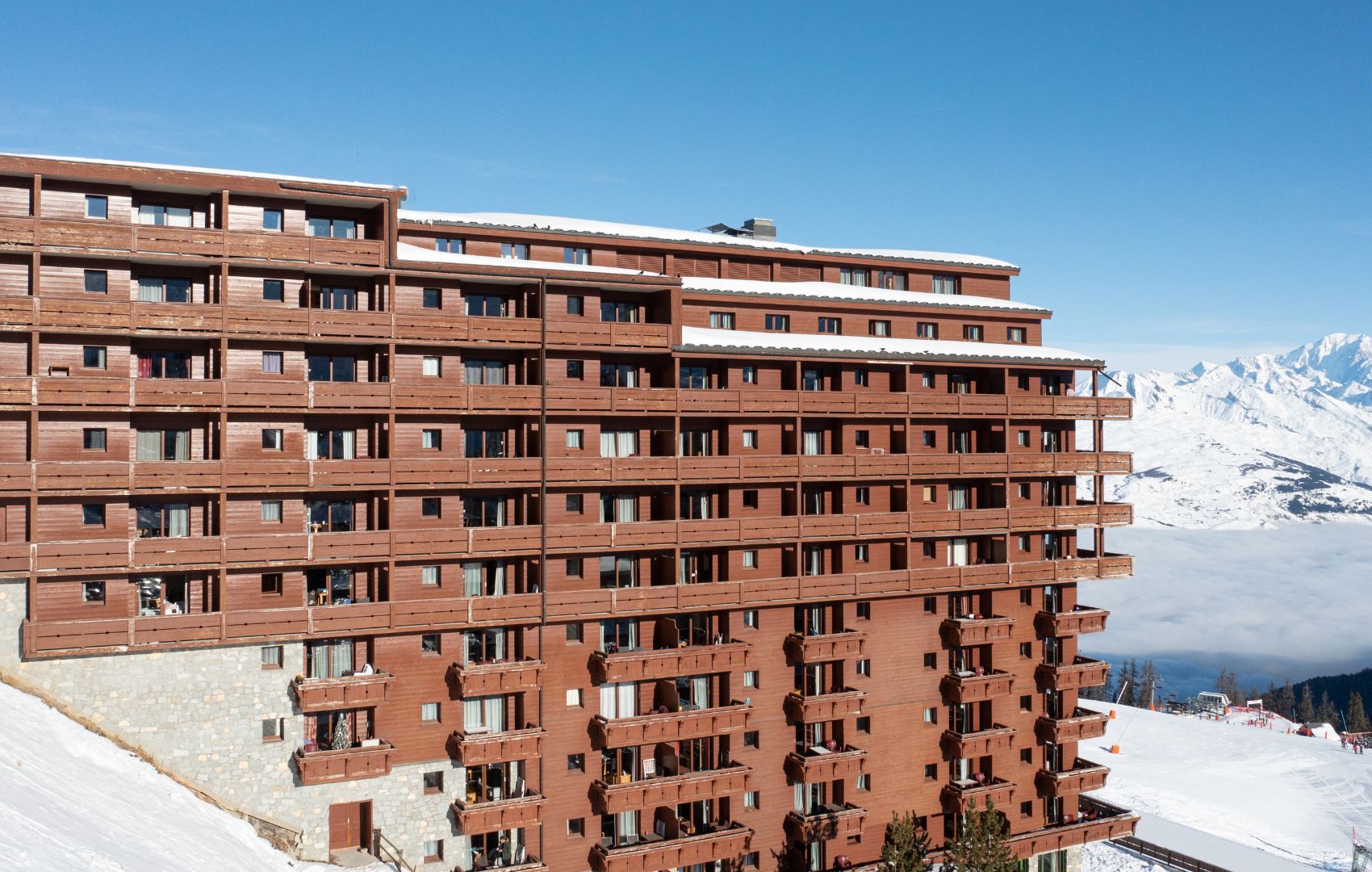 A multi-story hotel with a modern architectural design, featuring balconies and a ski resort backdrop.