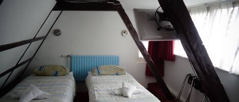 Una habitación con dos camas, un radiador azul y una ventana con cortinas rojas.