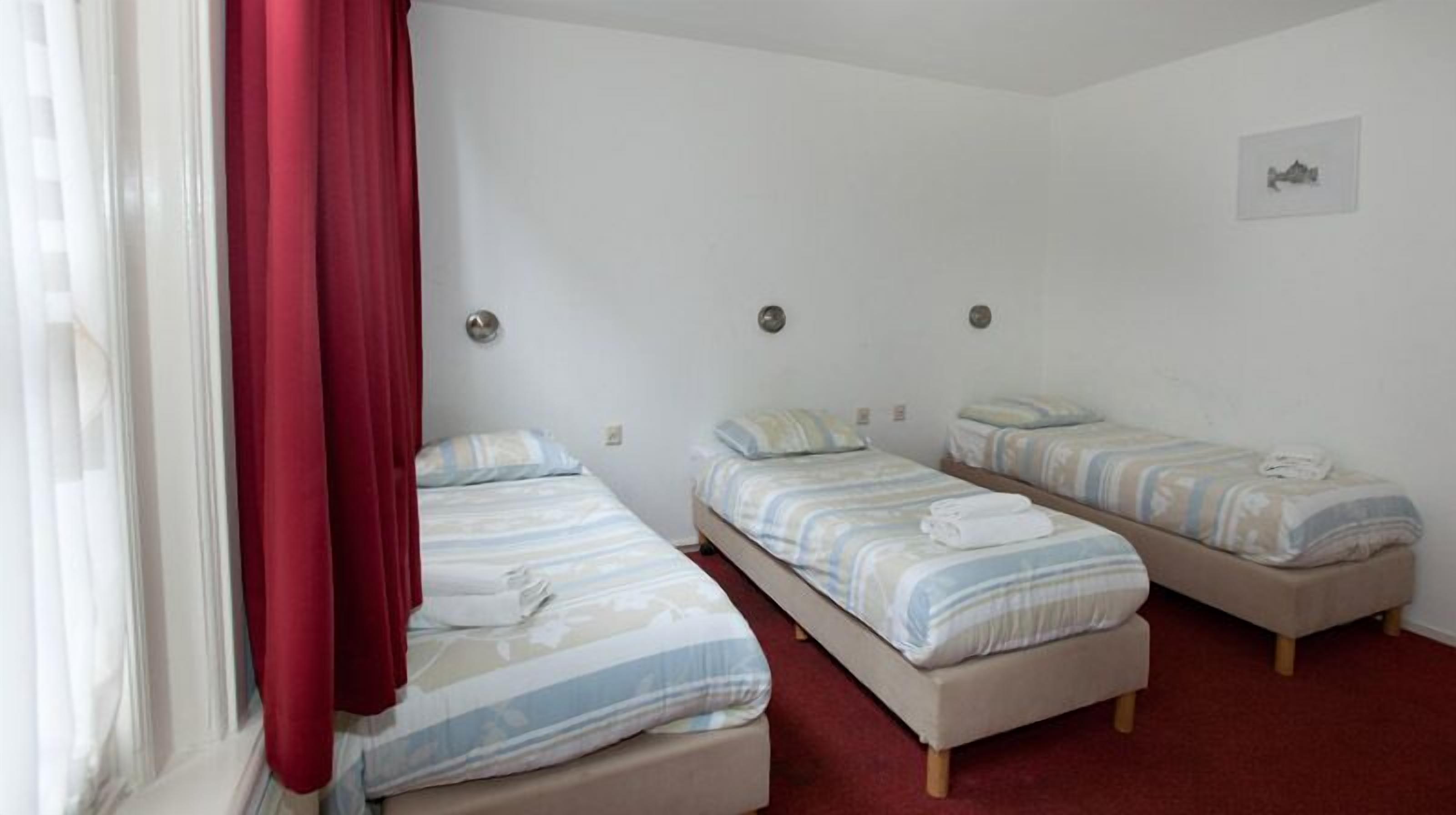 A room with three single beds, each with striped bedding and pillows, a red curtain, and a small picture on the wall.