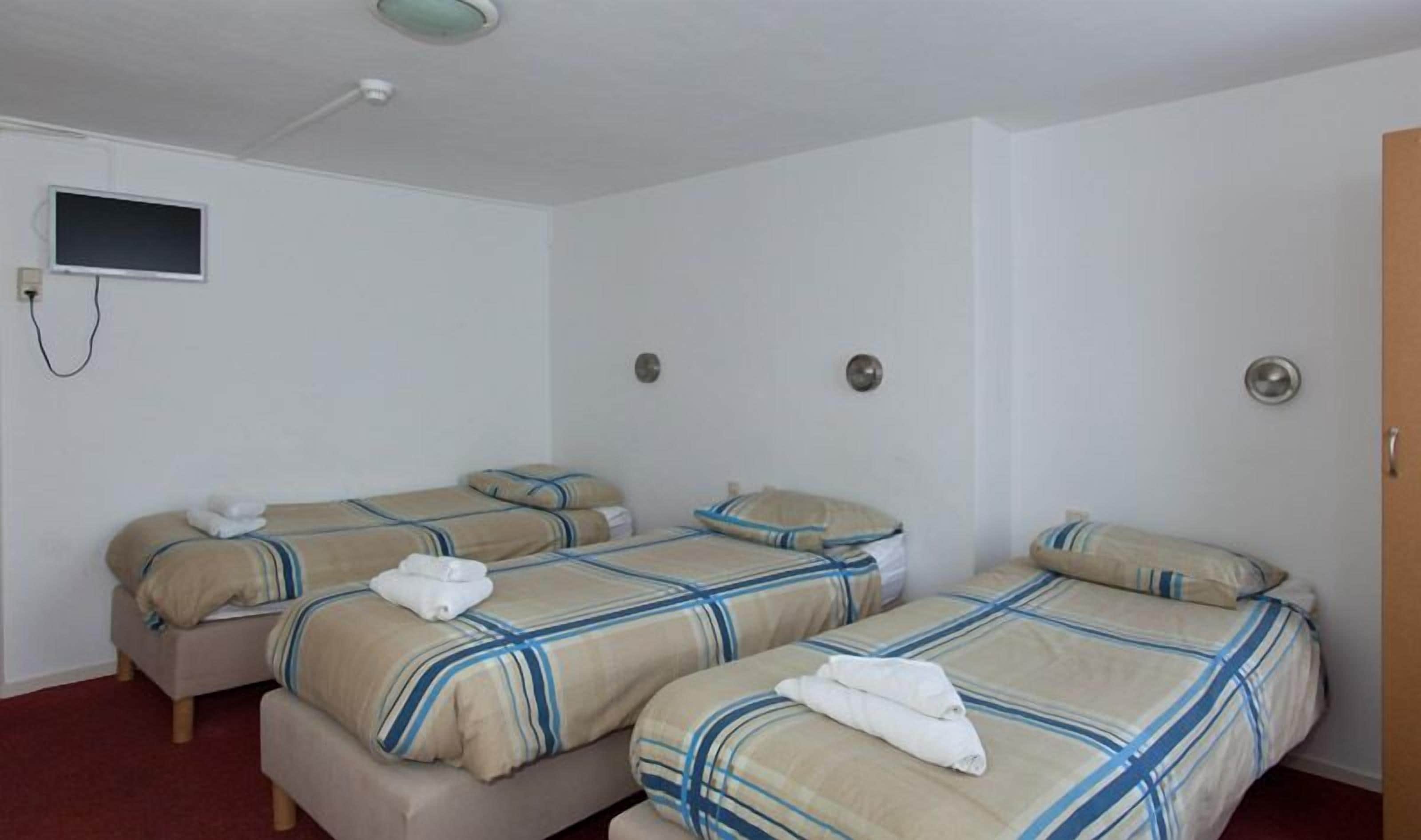 A hotel room with two beds, each with striped bedding and a folded towel. There is a television mounted on the wall and a door on the right.