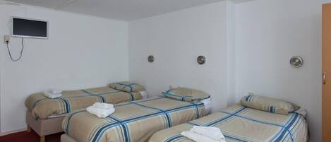 A hotel room with two beds, each with striped bedding and a folded towel. There is a television mounted on the wall and a door on the right.