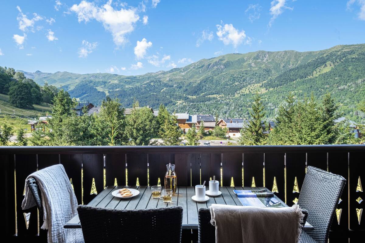 A terrace with a table set for dining, overlooking a mountainous landscape.