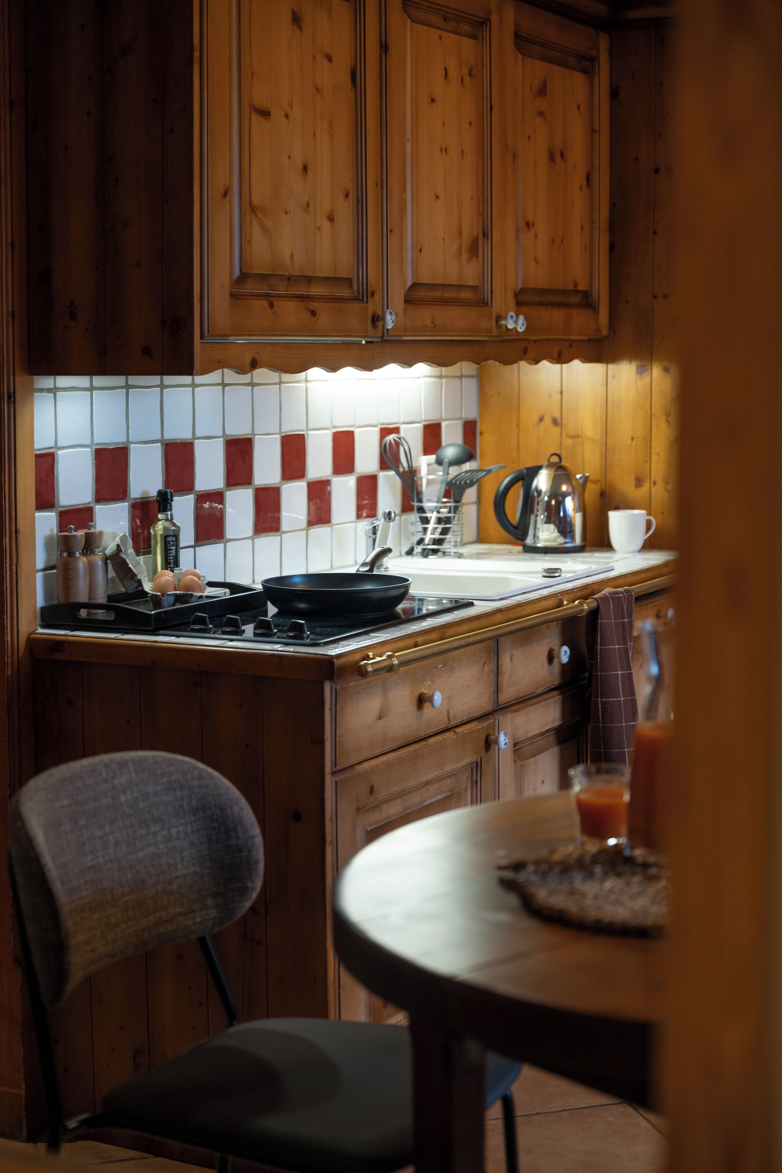 A kitchen with wooden cabinets, a tiled backsplash, a stove, and a dining area with a chair and table.