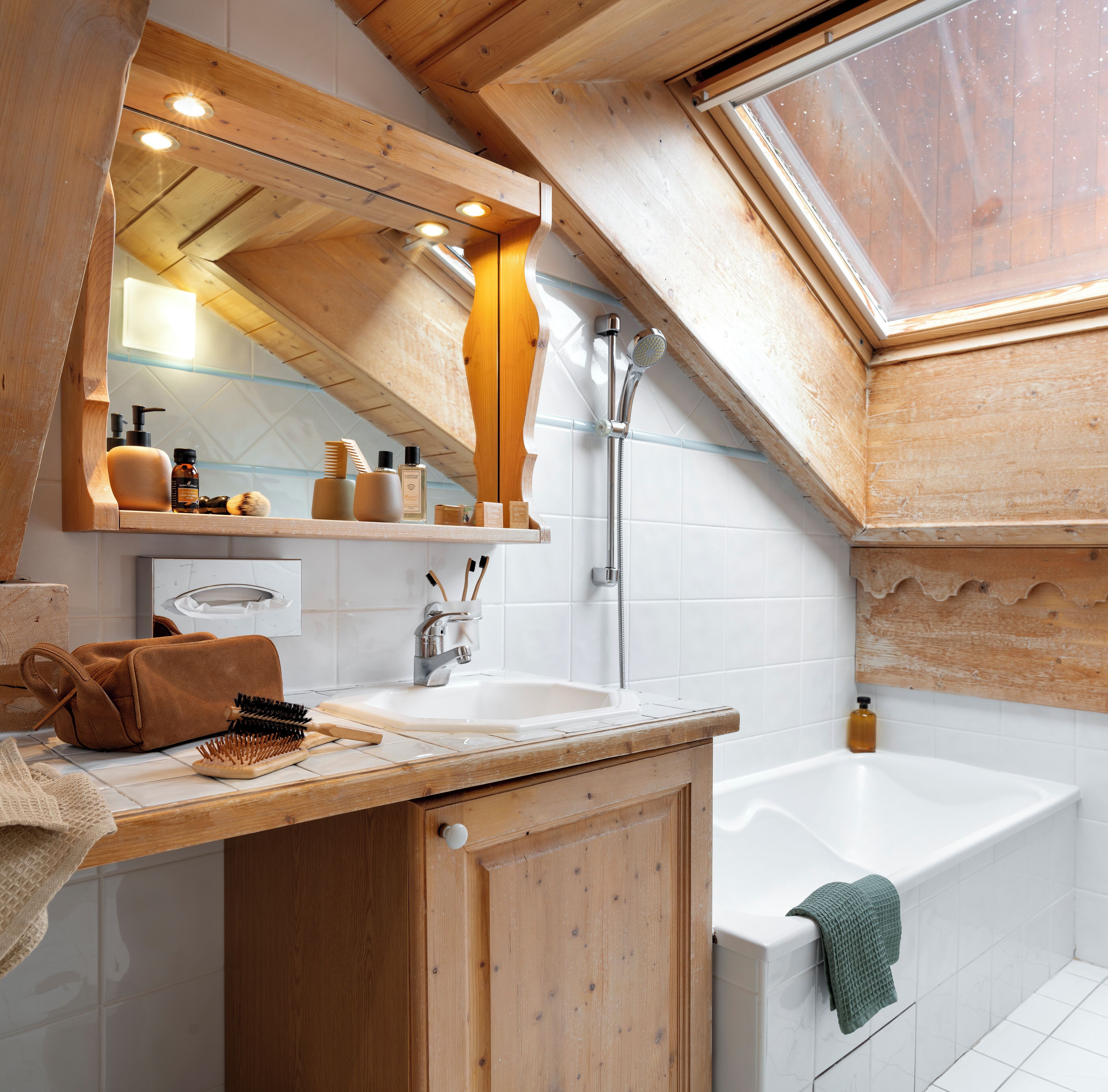 Une salle de bain avec un meuble-lavabo en bois, un grand miroir, une douche et une lucarne.