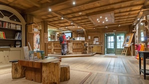 A rustic wooden interior with a reception desk, wooden tables, and a bookshelf. - Résidence Pierre & Vacances Premium Les Fermes de Méribel (Les Allues)