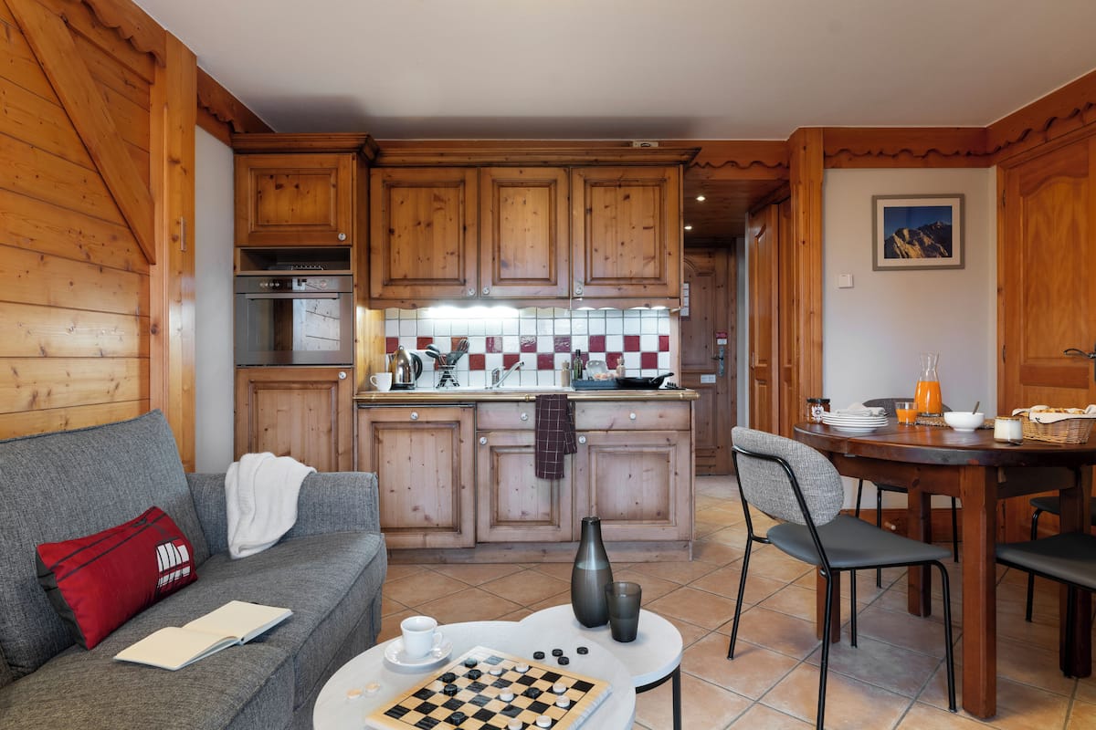 A cozy living room with a sofa, a coffee table with a chessboard, and a dining area with a table and chairs.