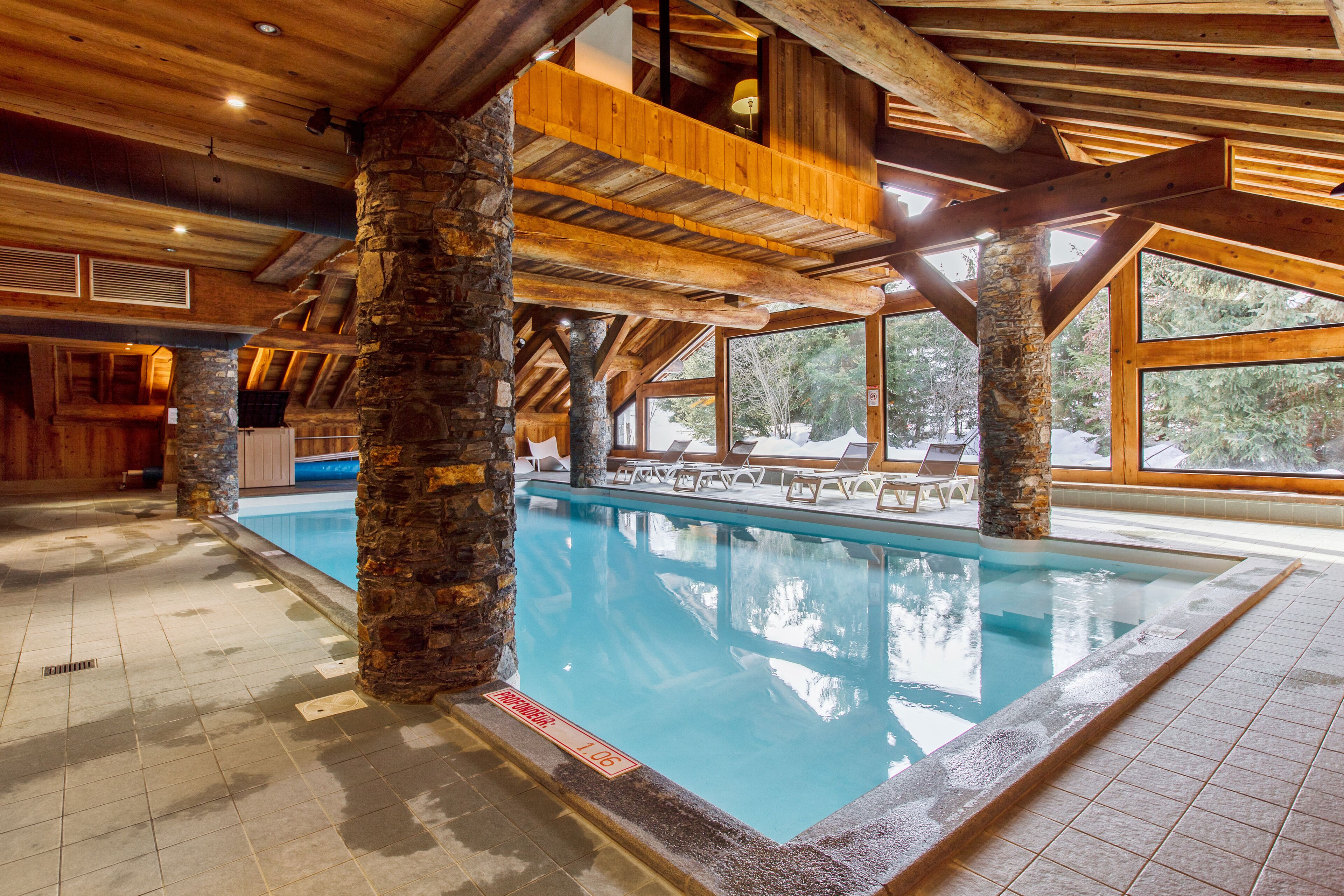 An indoor swimming pool with stone pillars, wooden beams, and large windows.