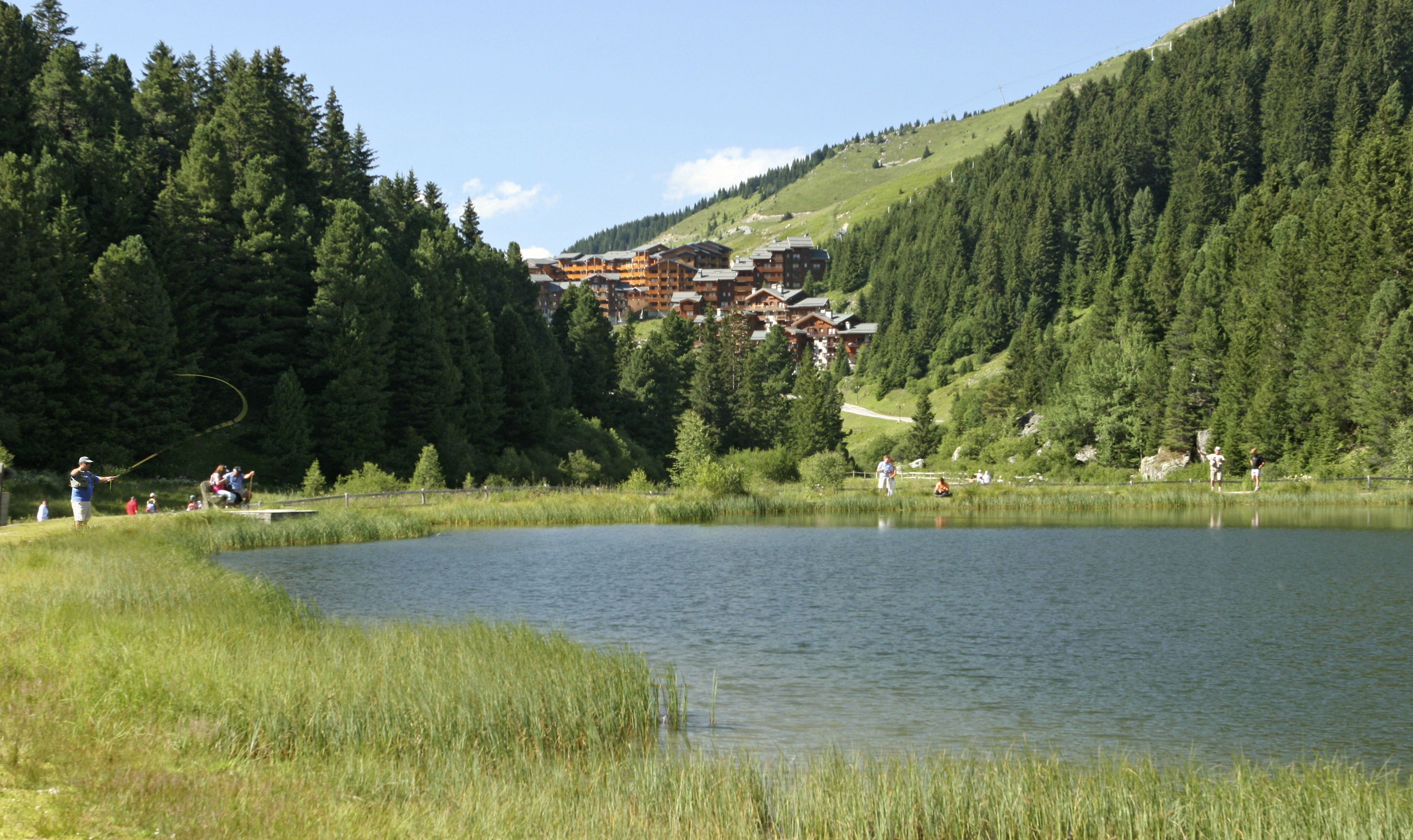 A lakeside view with a building complex in the background surrounded by dense forest.