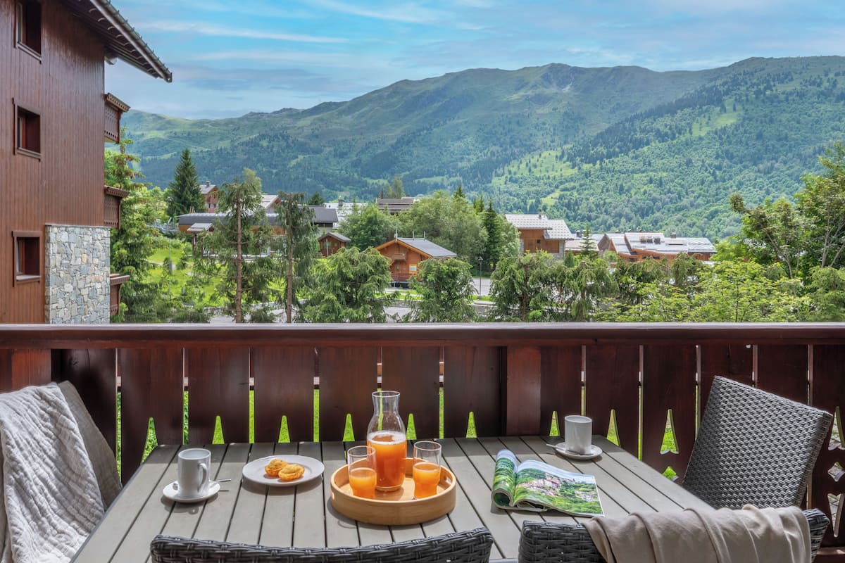 A wooden deck with a table set for breakfast, overlooking a mountainous landscape.