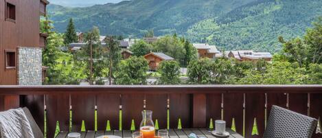 Une terrasse en bois avec une table dressée pour le petit-déjeuner, offrant une vue sur un paysage montagneux.