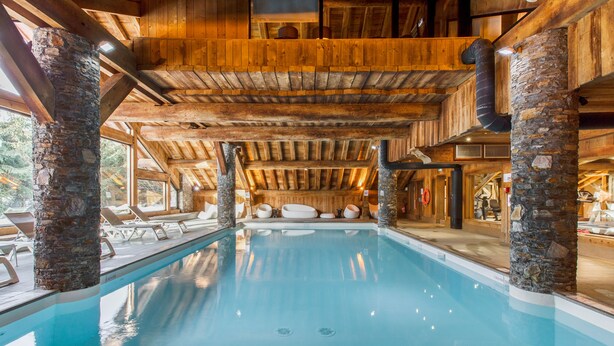 An indoor swimming pool with stone pillars, wooden beams, and a view of the surrounding area. - Résidence Pierre & Vacances Premium Les Fermes de Méribel (Les Allues)
