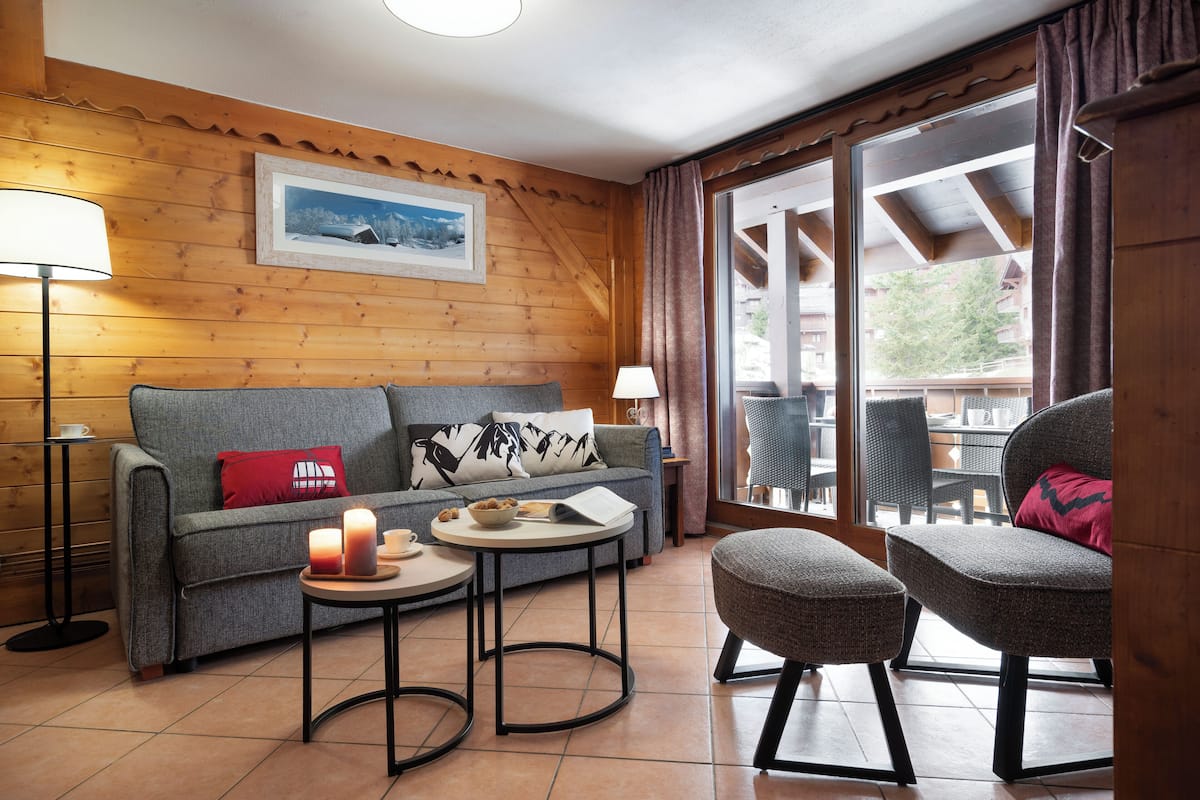 A cozy living room with a sofa, two side tables, a lamp, and a view of the outdoors.