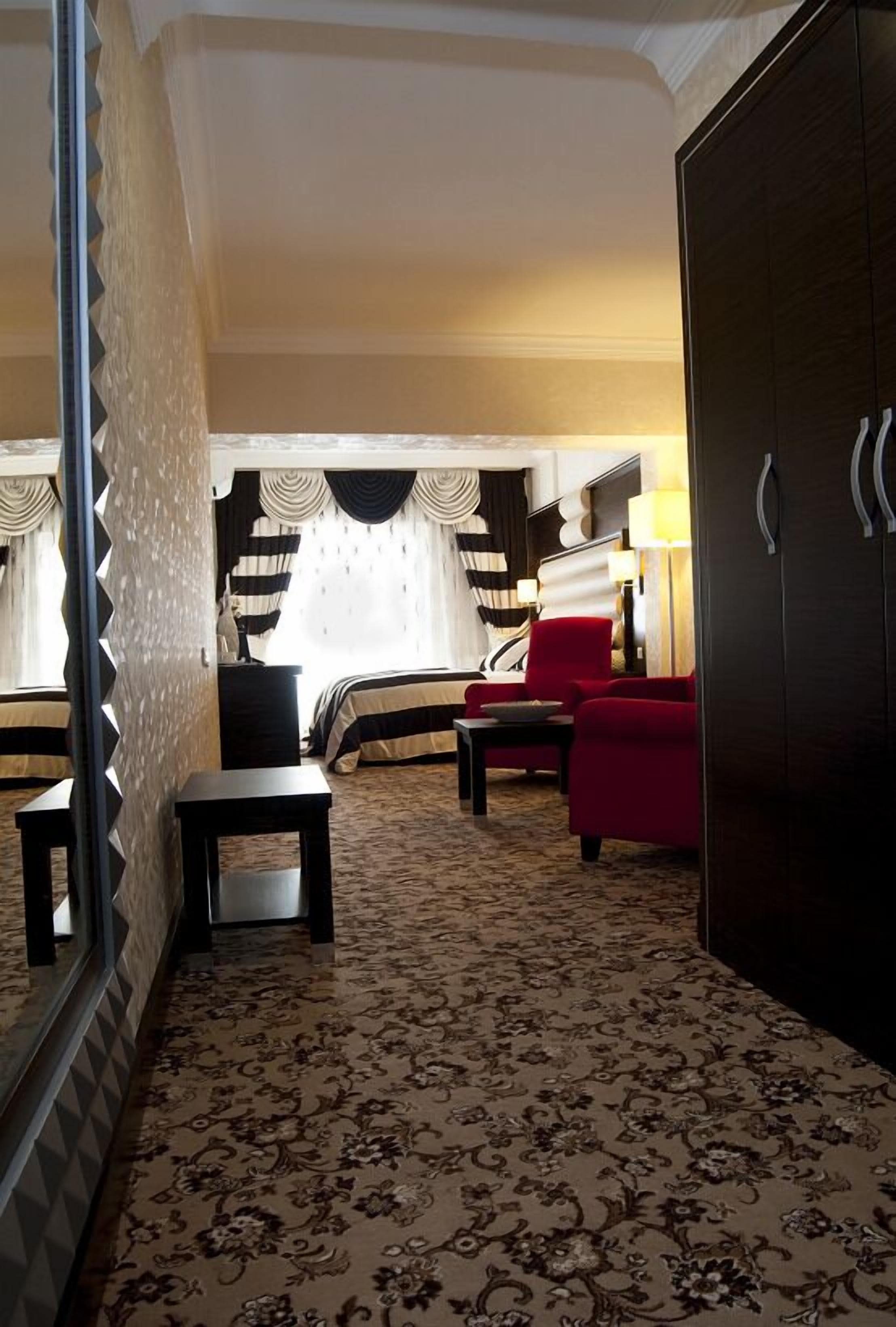 A hotel room with a bed, two red armchairs, a small table, and a wardrobe.